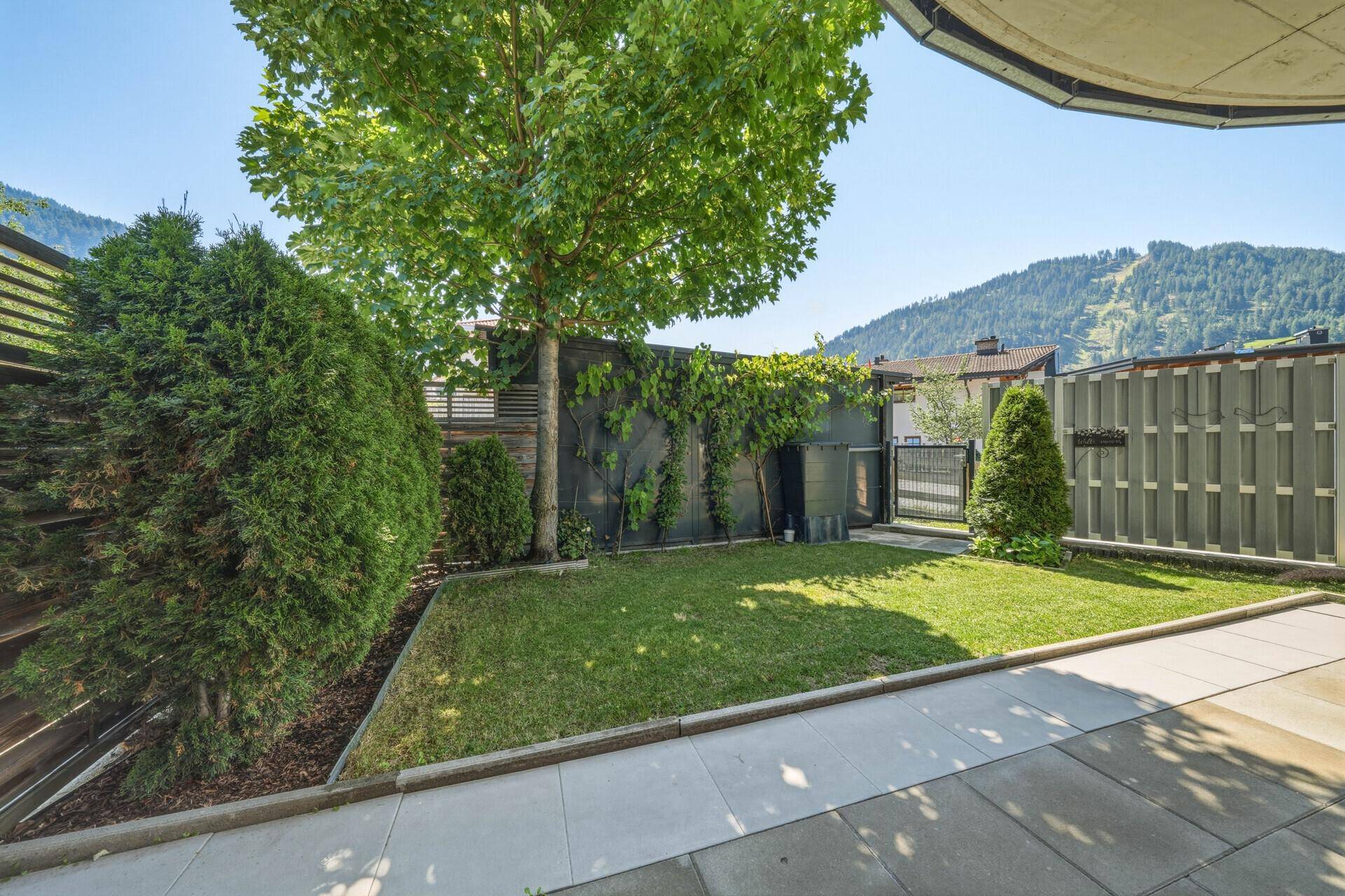 Kleiner, gepflegter Gartenbereich mit Rasen, Bäumen und Bergblick.
