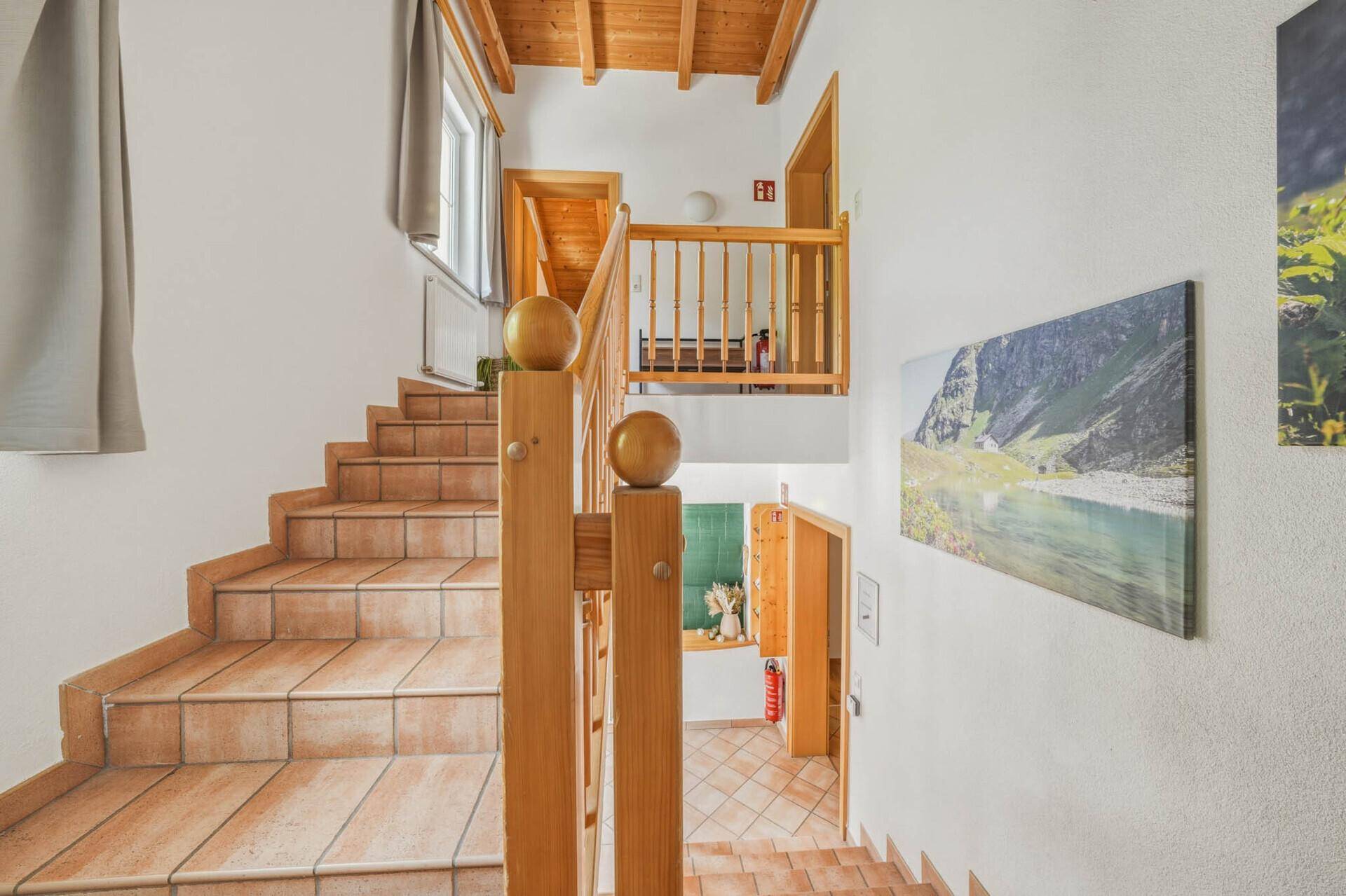Holztreppe mit gefliesten Stufen und Holzdecke, die die verschiedenen Ebenen verbindet.