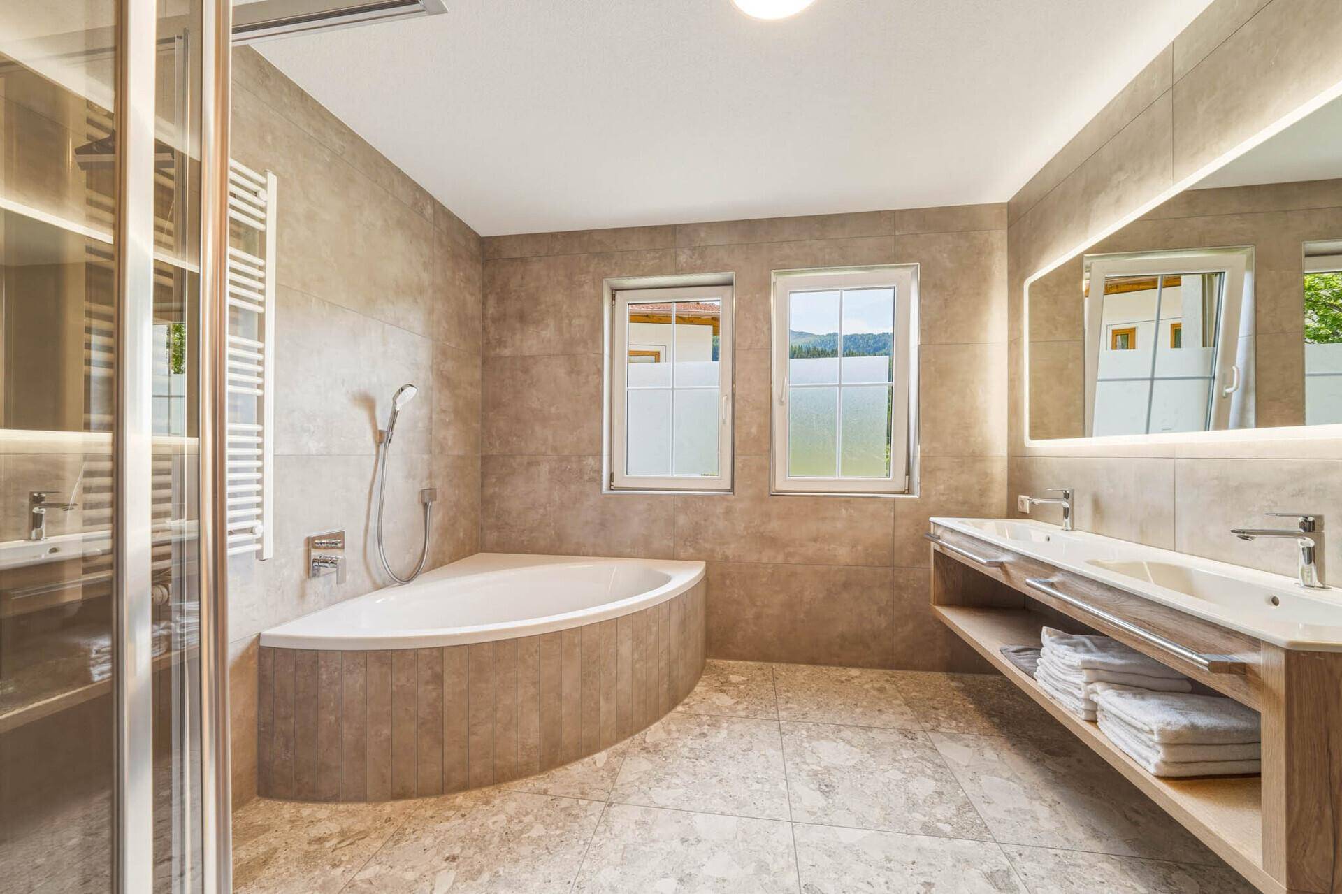 Modernes Badezimmer mit Eckbadewanne, Dusche, Doppelwaschbecken und beleuchtetem Spiegel.