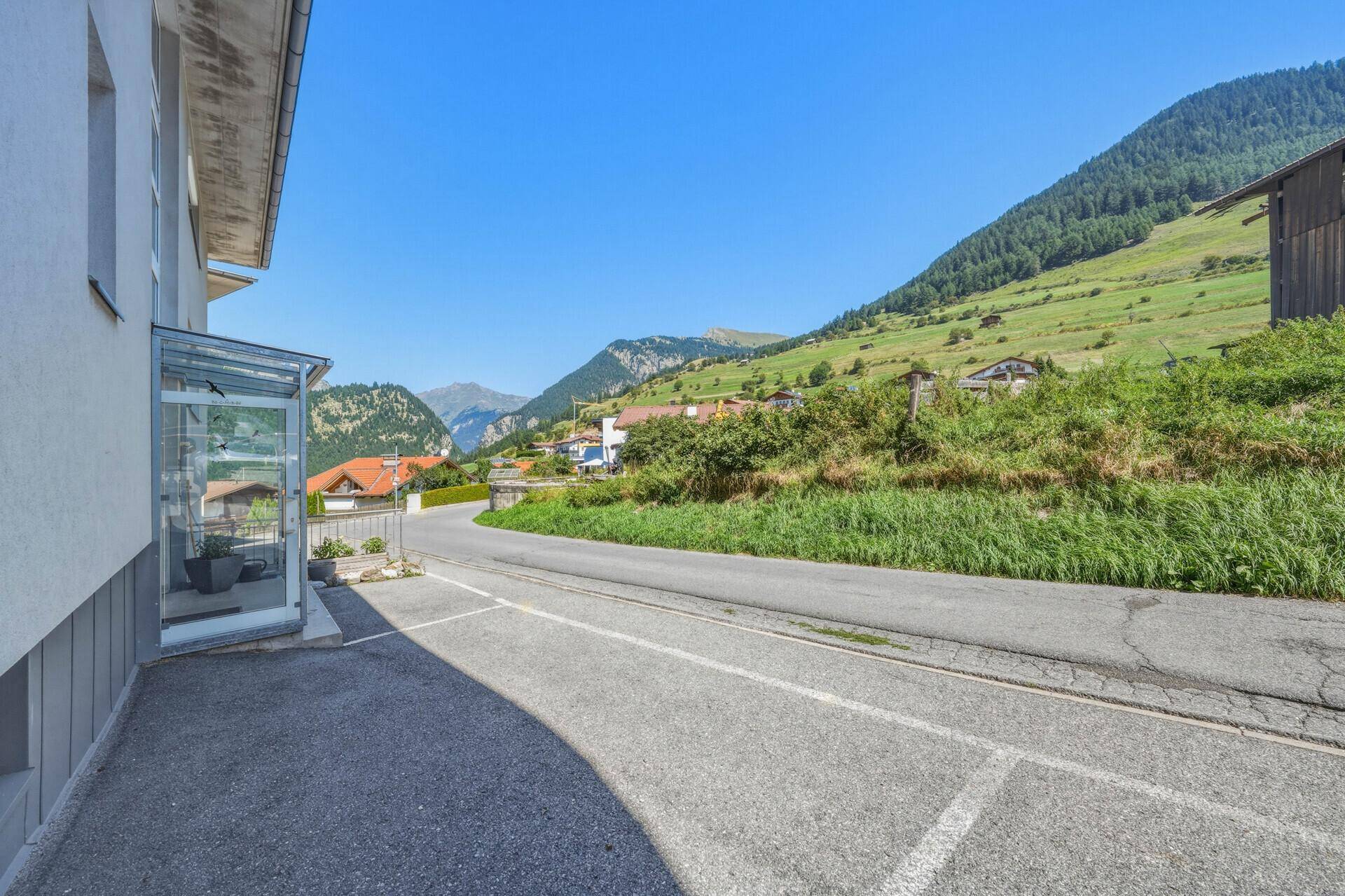 Straße vor dem Gebäude mit Blick auf die umliegende grüne Hügellandschaft und Berge.