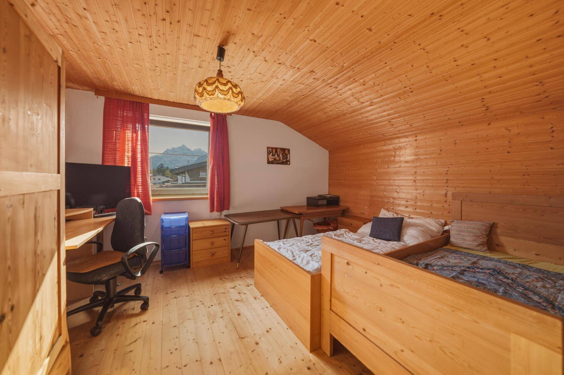 Schlafzimmer im Dachgeschoss mit Holzverkleidung, Einzelbetten und Schreibtisch.