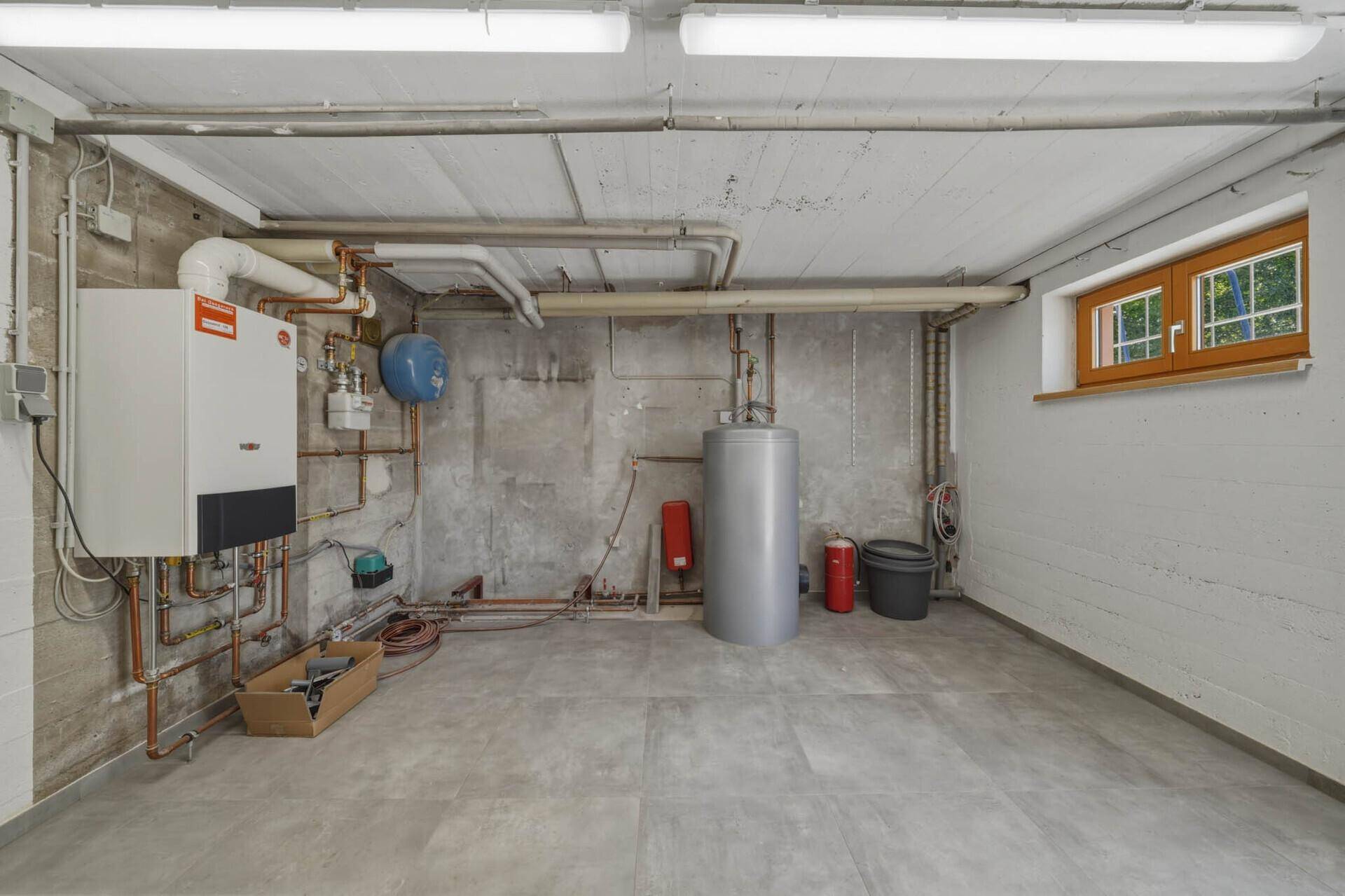 Heizungsraum im Keller mit moderner Heizungsanlage, Warmwasserspeicher und Fliesenboden.