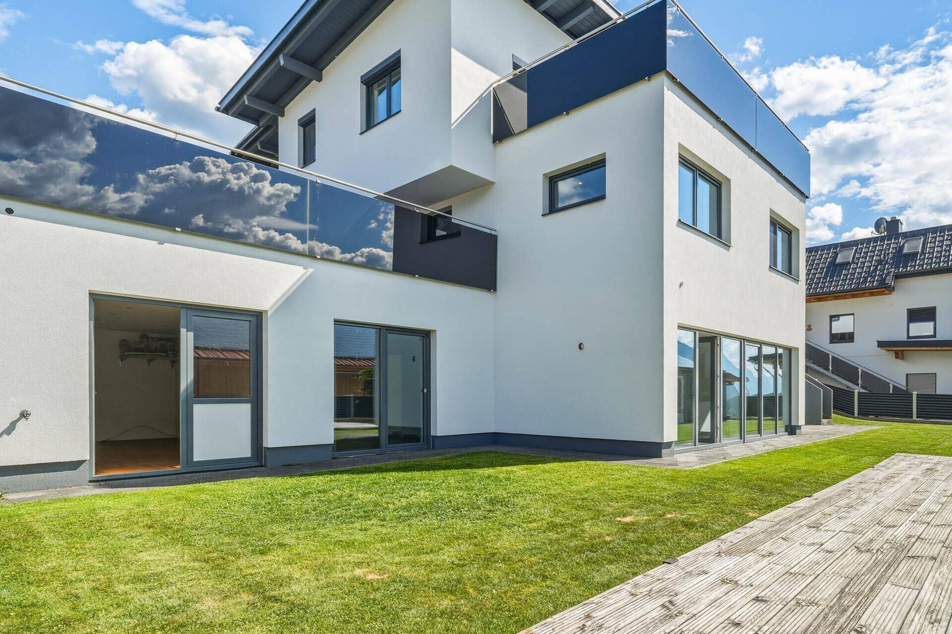 Seitenansicht des modernen Hauses mit Glasbalkonen und gepflegter Rasenfläche.