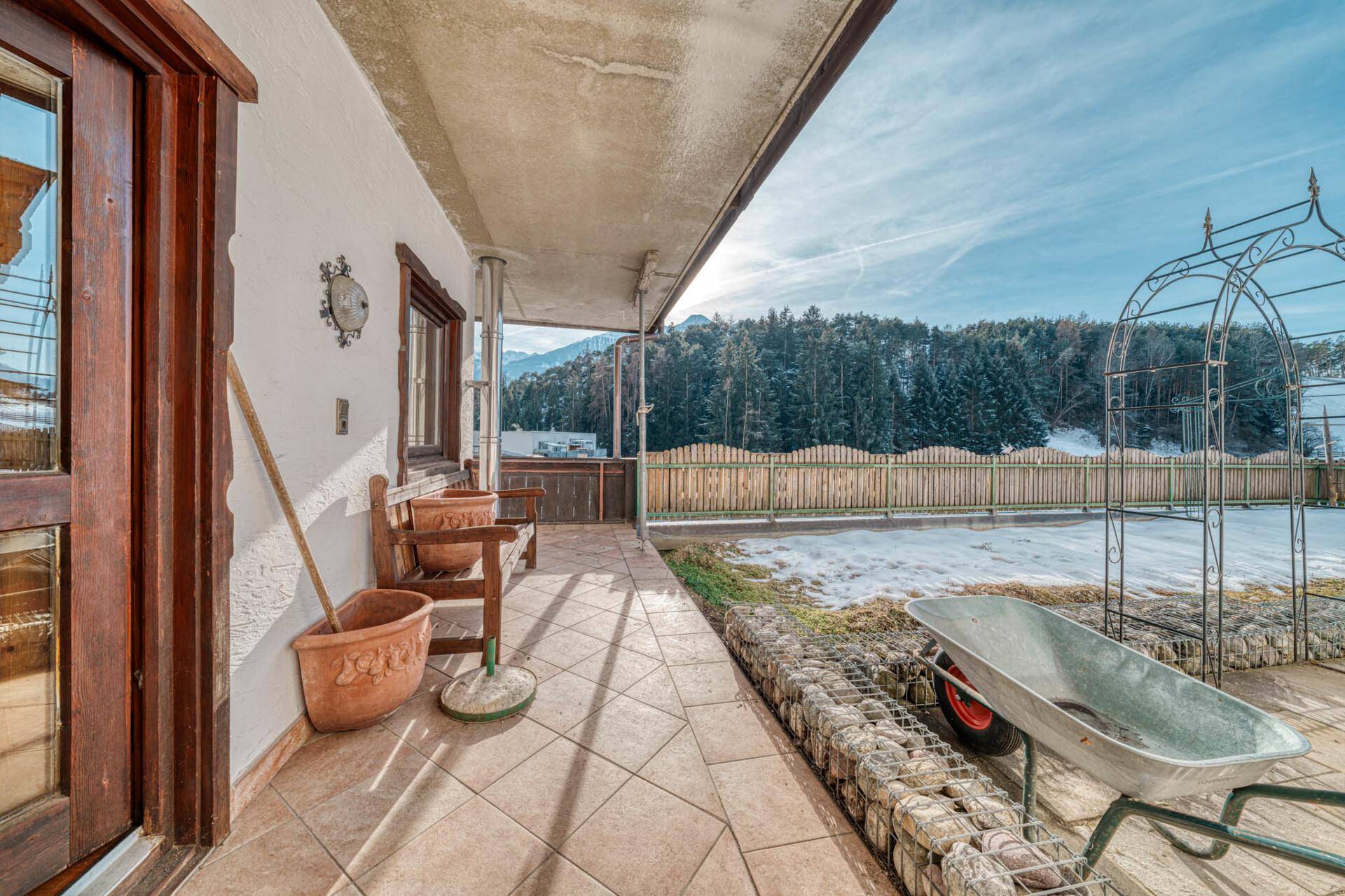 Überdachte Terrasse mit Fliesenboden und Blick auf den Garten und die verschneite Landschaft.