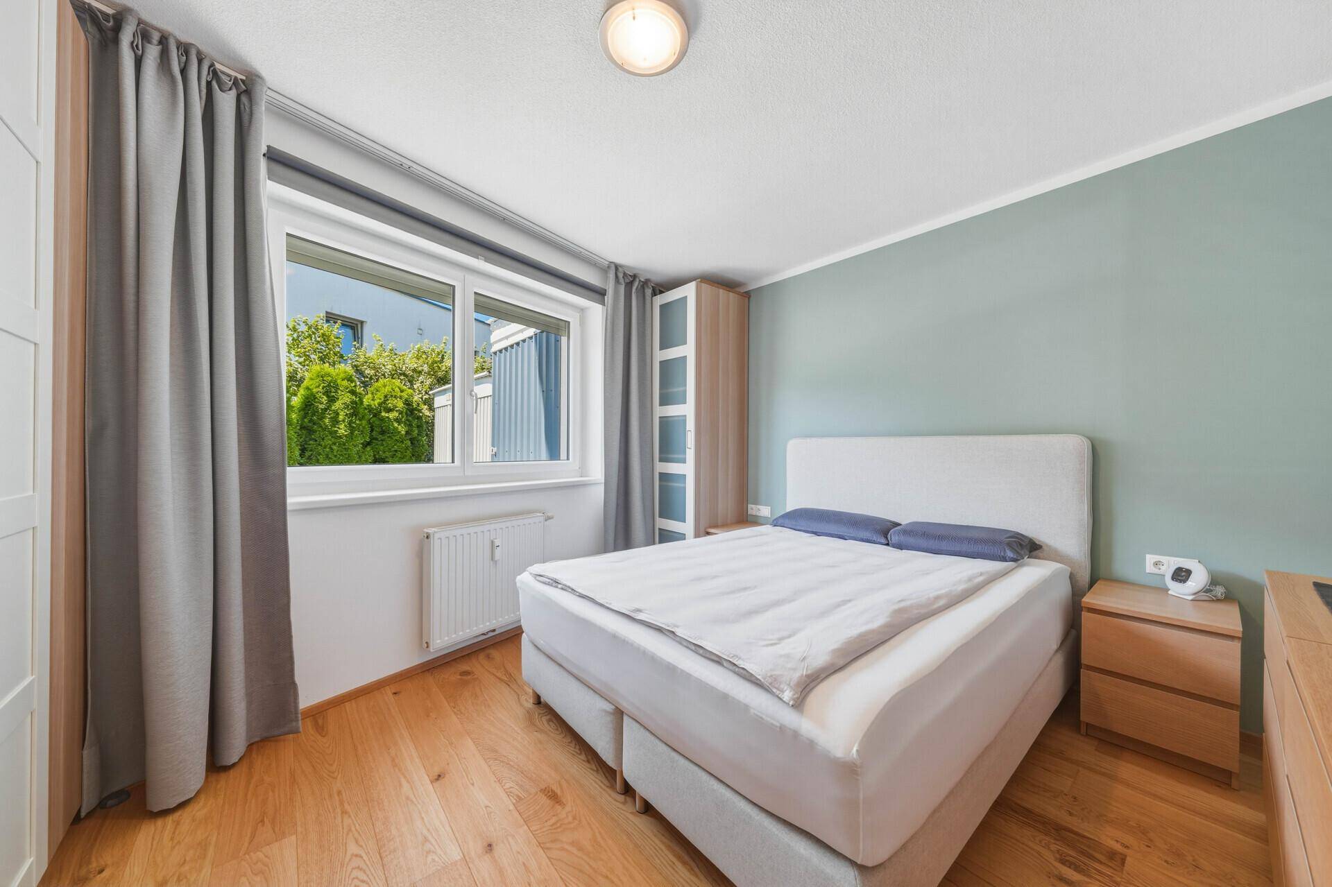 Gemütliches Schlafzimmer mit Doppelbett, Holzboden und Fenster mit Blick ins Grüne.