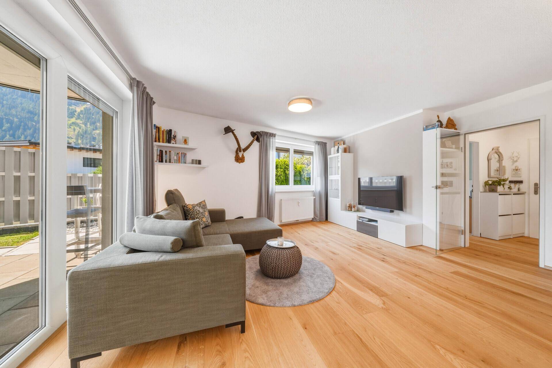 Helles Wohnzimmer mit Holzboden, bequemer Couch und Blick in den Eingangsbereich.