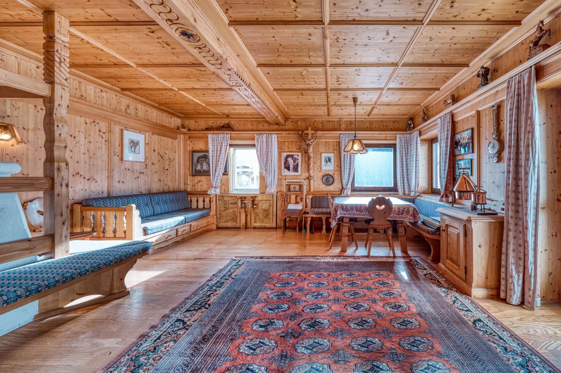 Traditioneller Wohn-Essbereich im alpinen Stil mit viel Holz, Teppich und gemütlicher Atmosphäre.