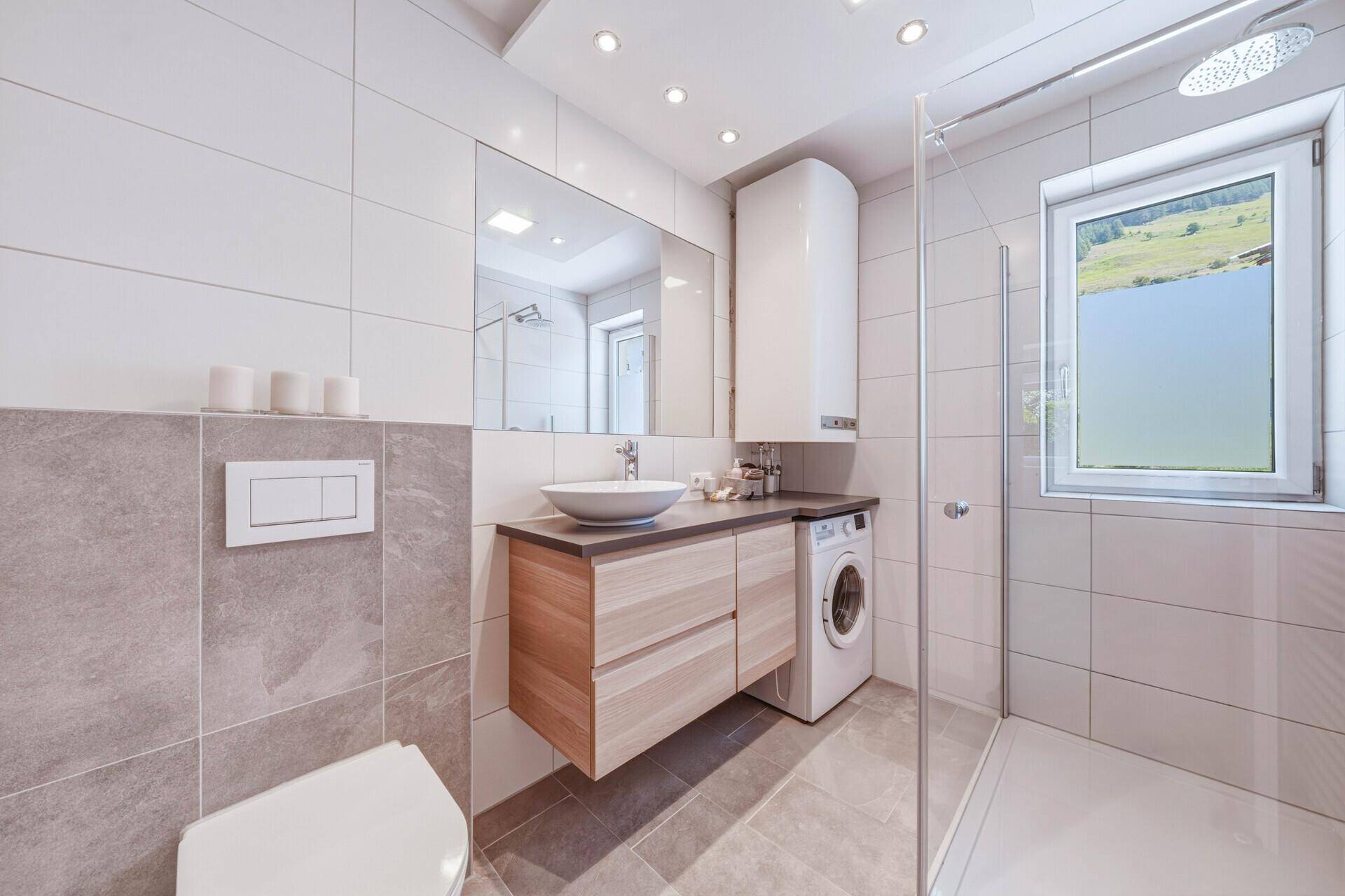 Helles Badezimmer mit modernen Fliesen, Waschbecken und integrierter Waschmaschine.