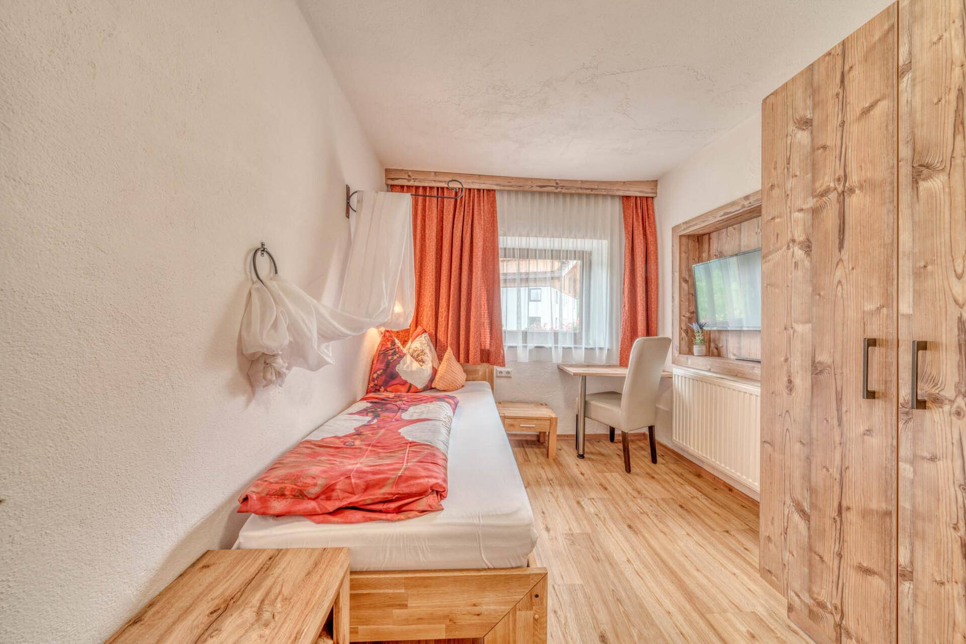 Helles Schlafzimmer mit Einzelbett, Holzschrank und Schreibtisch, gemütlich eingerichtet.