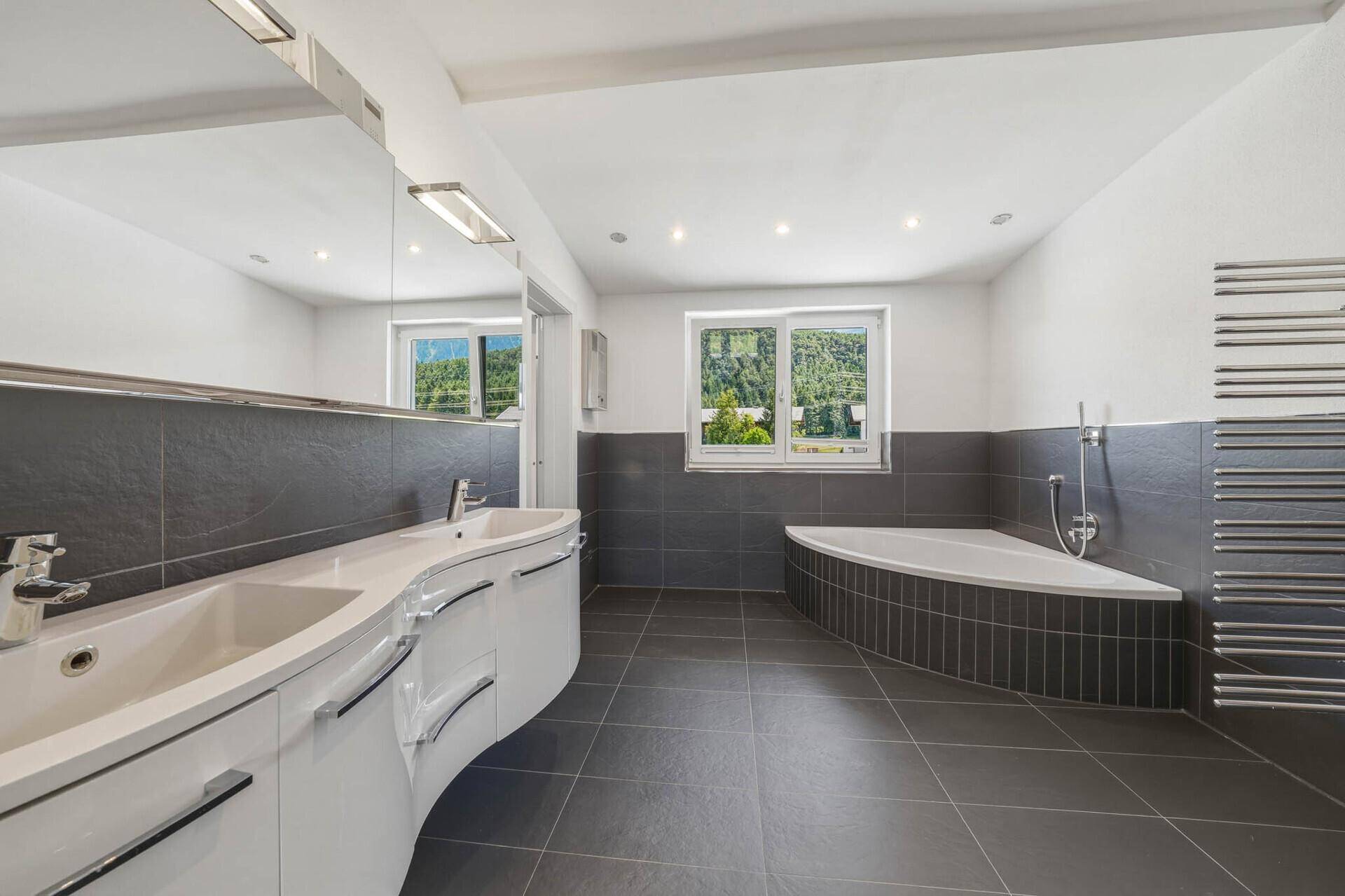 Großes modernes Badezimmer mit Doppelwaschbecken, Eckbadewanne und dunklen Fliesen.