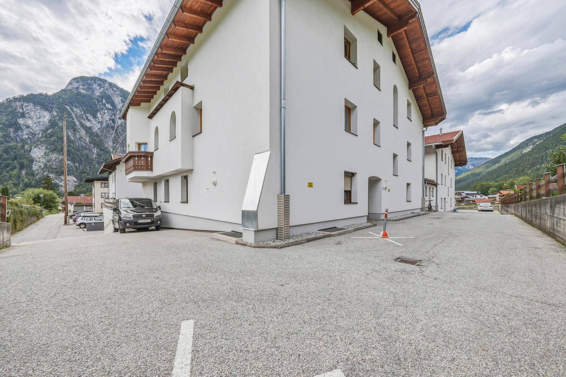 Gebäudeecke mit großem, gepflastertem Parkplatz und Blick auf die umliegenden Berge.