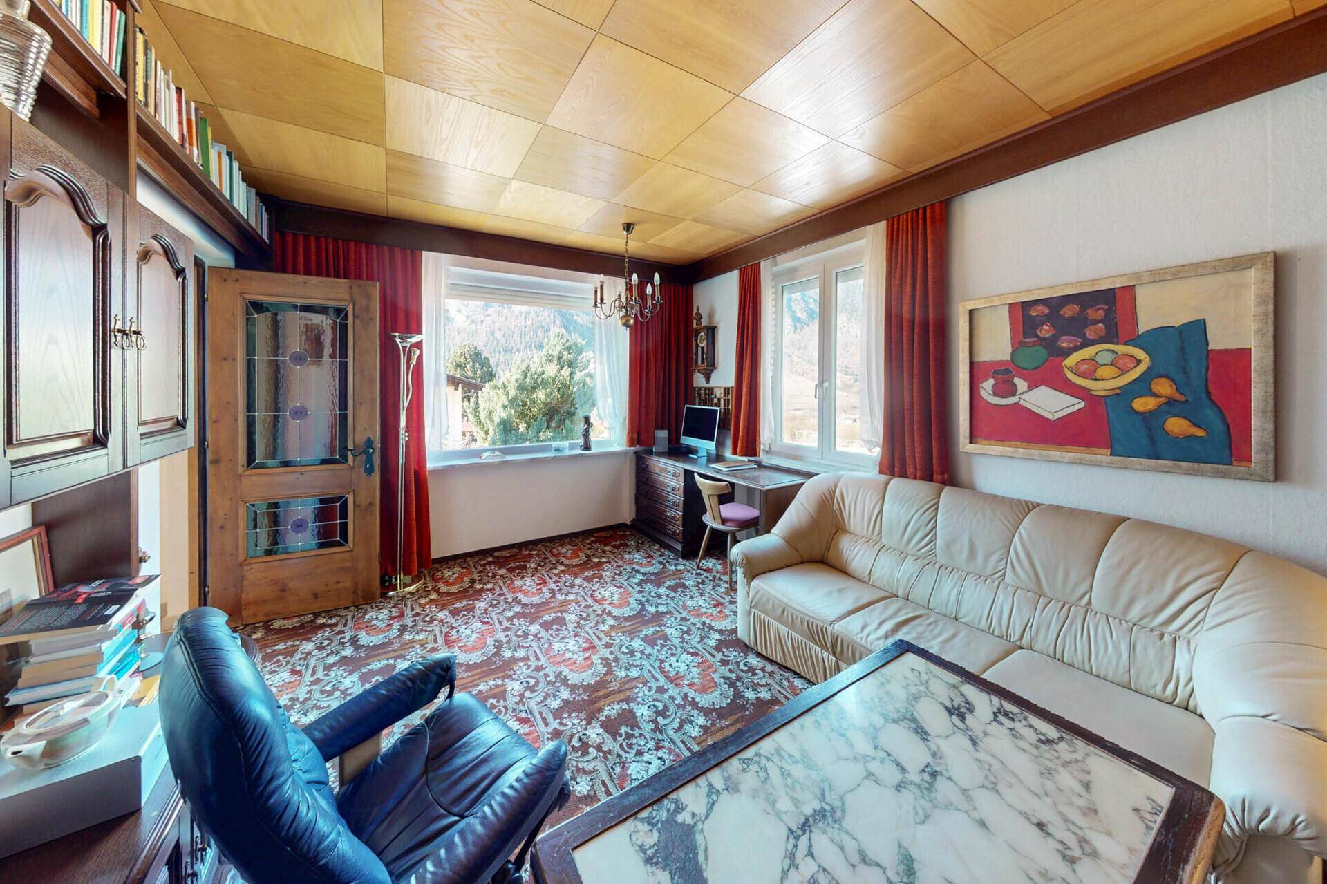 Traditionelles Wohnzimmer mit Holztäfelung, Teppichboden und Schreibtisch am Fenster.