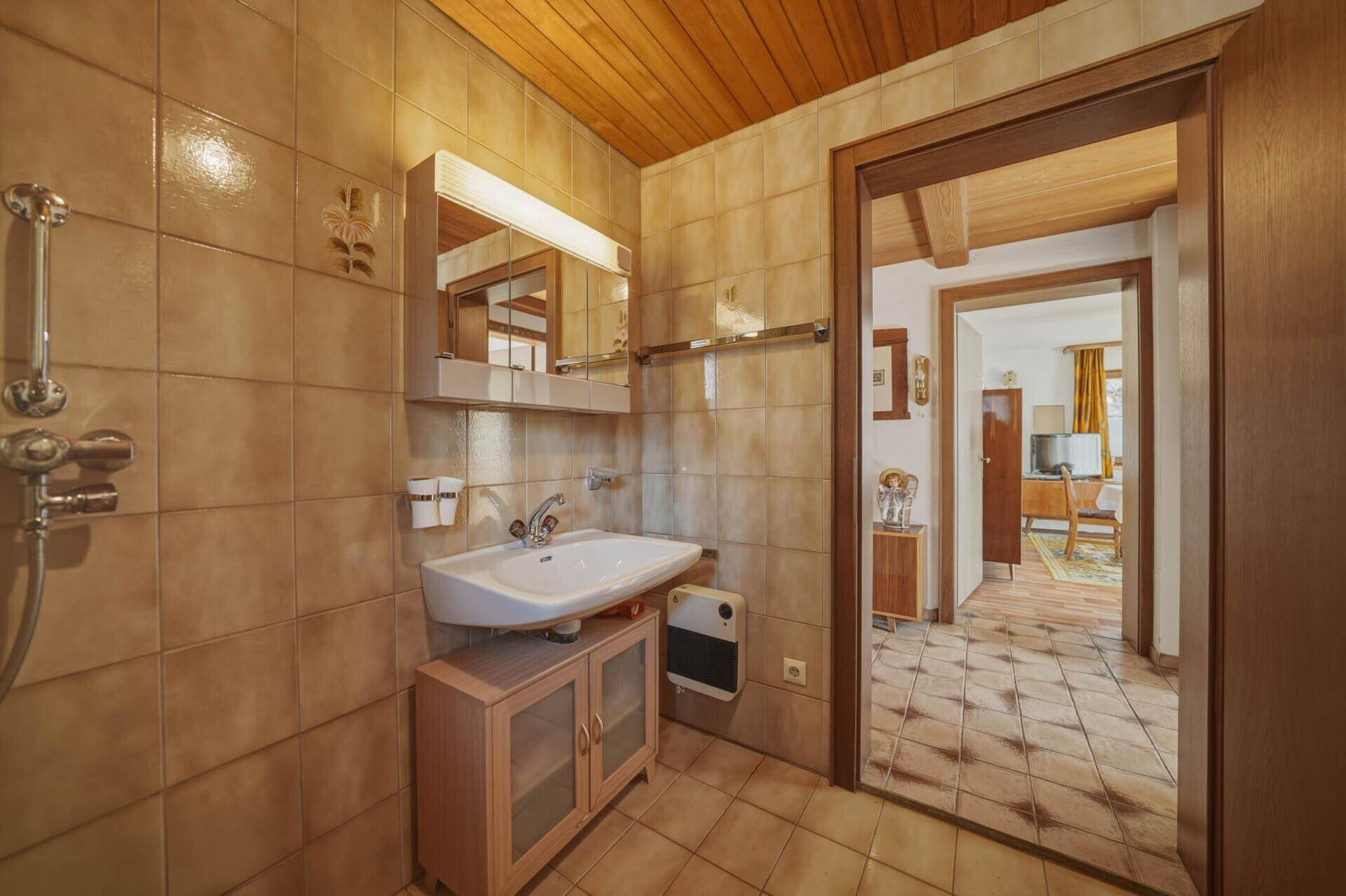 Badezimmer mit Waschbecken und Spiegelschrank, braunen Fliesen und Holzdecke.