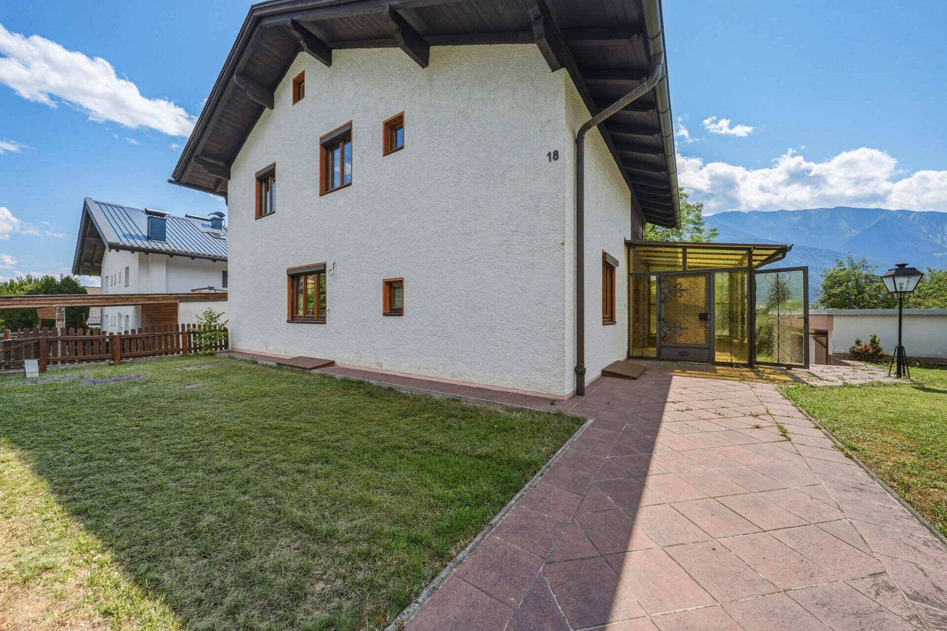 Seitenansicht des Hauses mit gepflastertem Weg, Rasen und Bergblick im Hintergrund.
