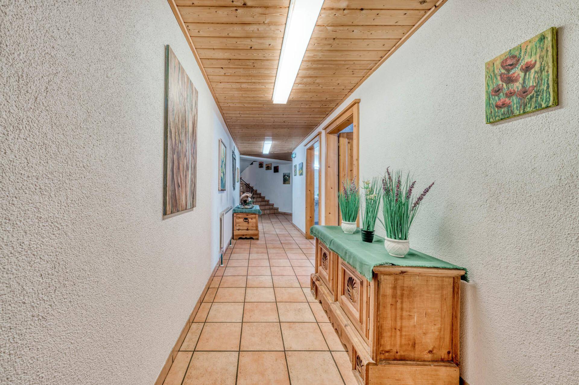 Langer Flur mit Fliesenboden, Holzdecke und traditionellen Möbeln und Bildern.