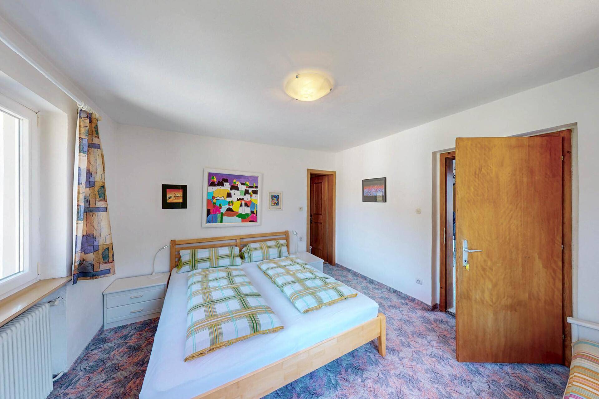 Helles Schlafzimmer mit Doppelbett, Teppichboden und Blick auf die Berge.