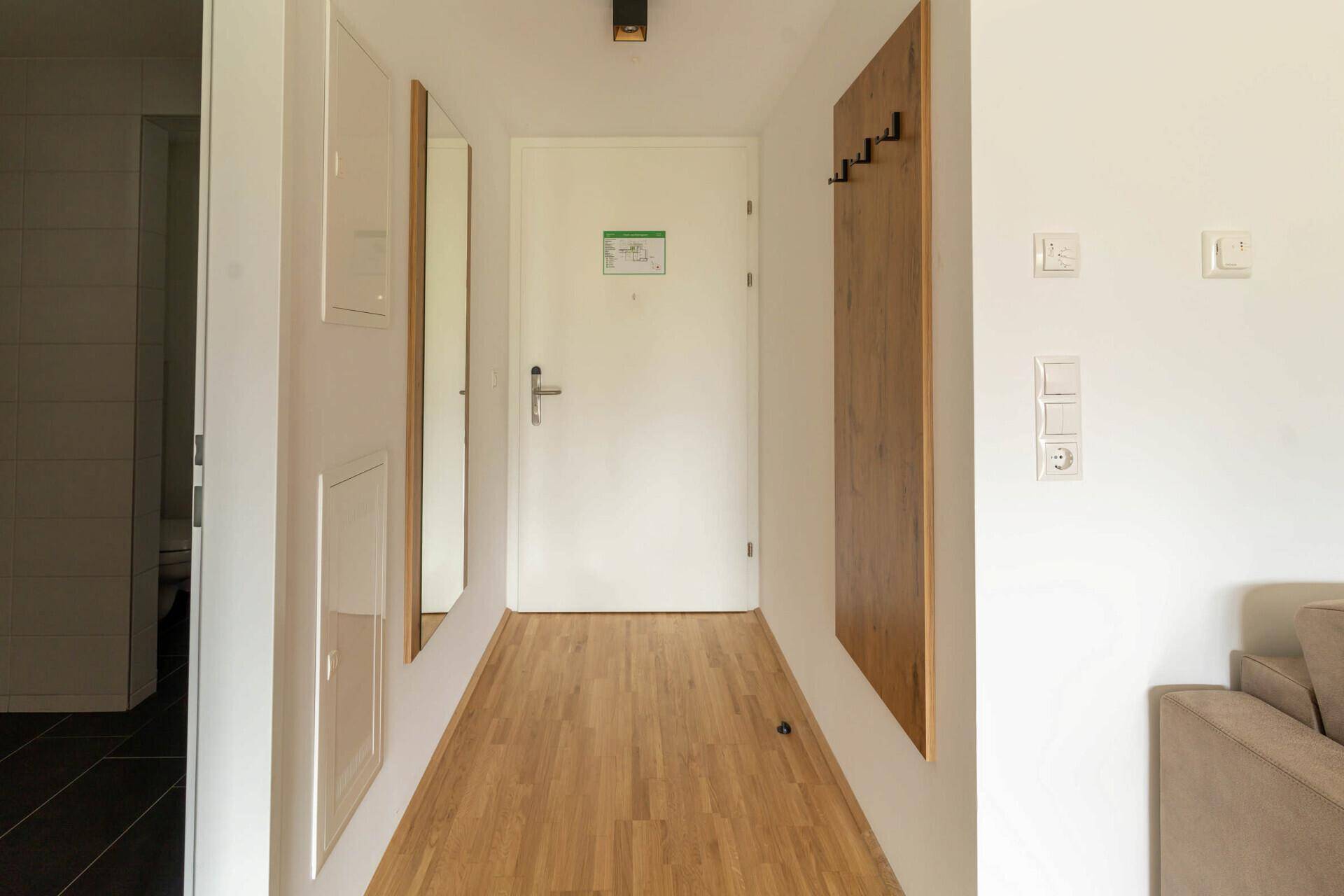 Heller Eingangsbereich mit Holzboden, Garderobe und Wandspiegel.
