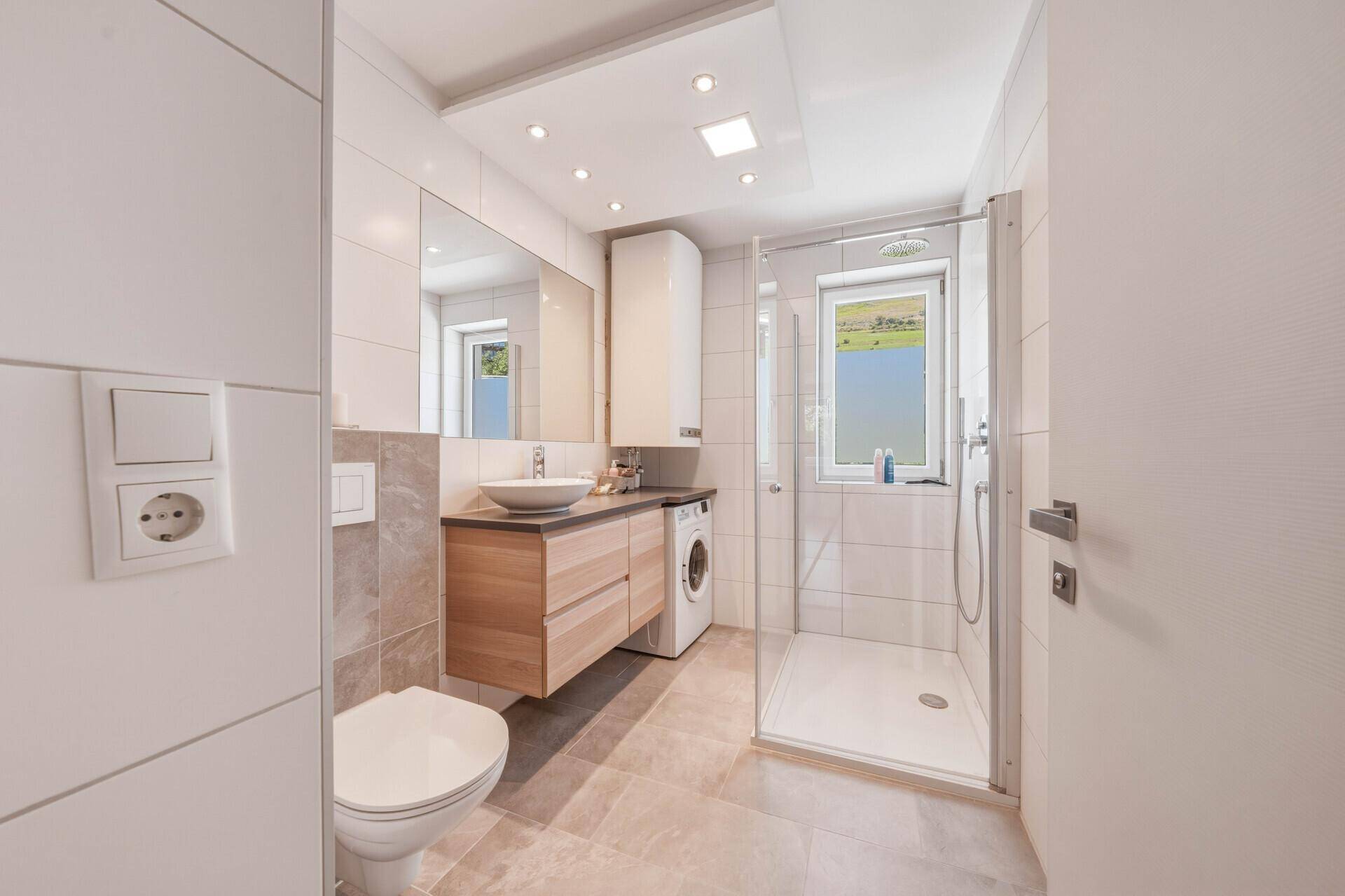 Modernes Badezimmer mit ebenerdiger Dusche, Waschmaschine und Fenster mit Bergblick.