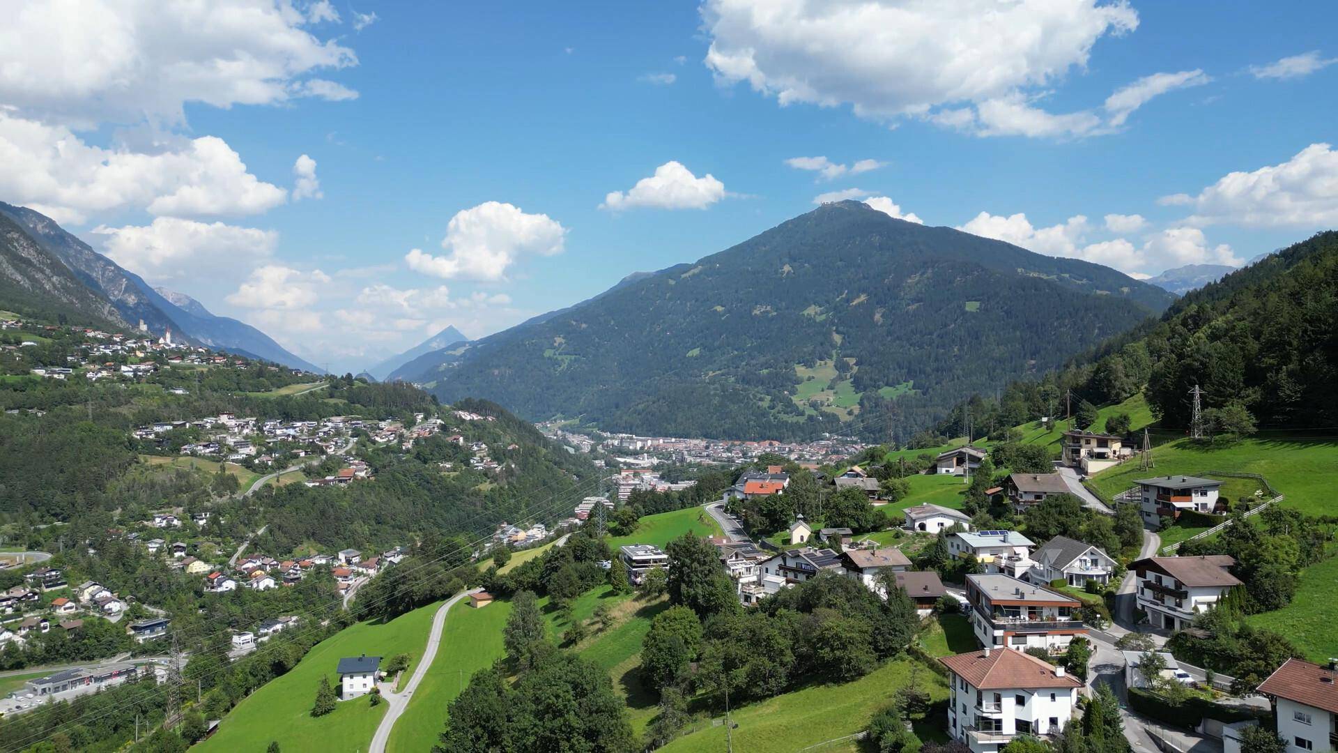 Panoramablick auf ein malerisches Bergdorf eingebettet in eine grüne Tallandschaft unter blauem Himmel.
