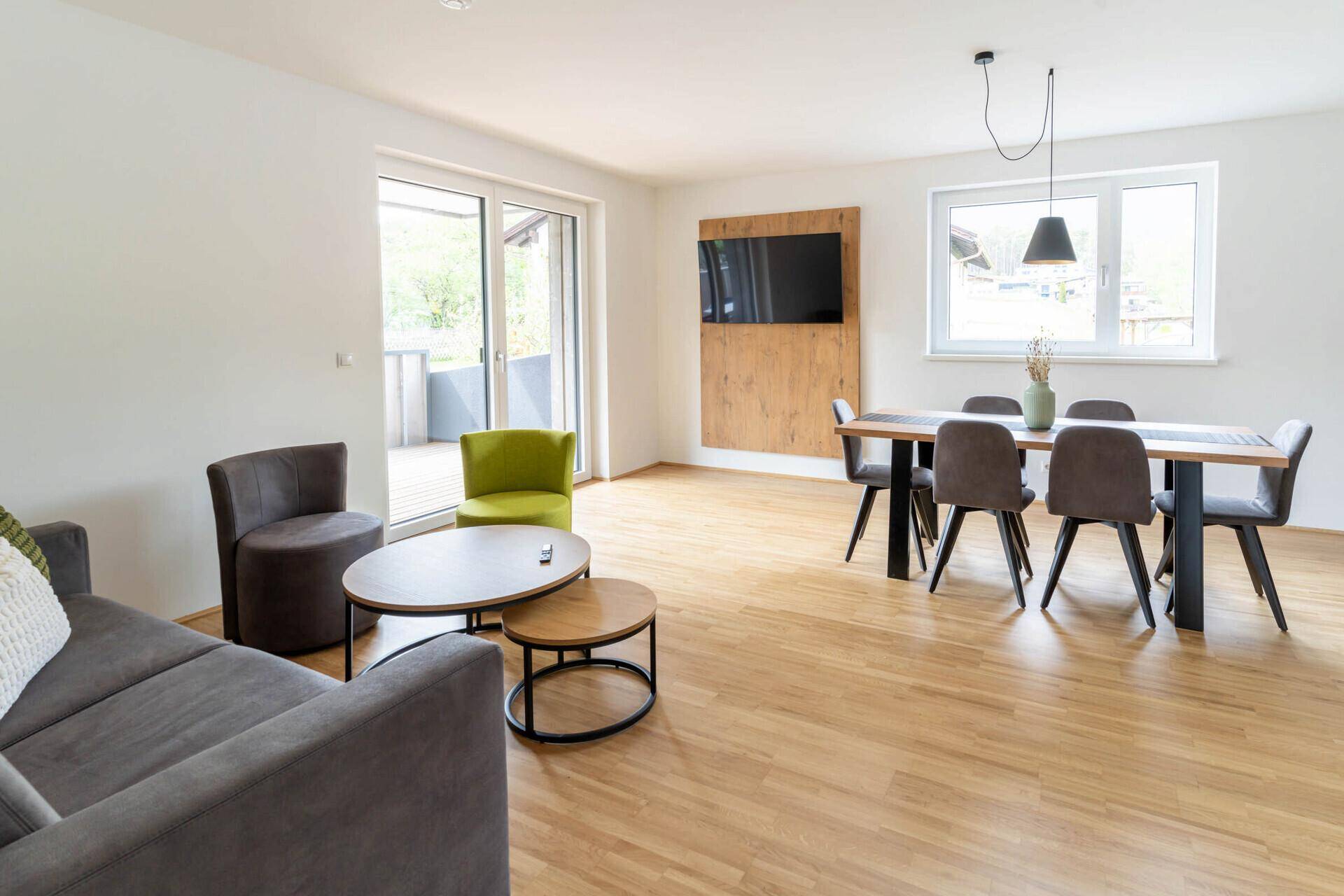 Heller Wohn-Essbereich mit Holzboden, Esstisch und Zugang zum Balkon.