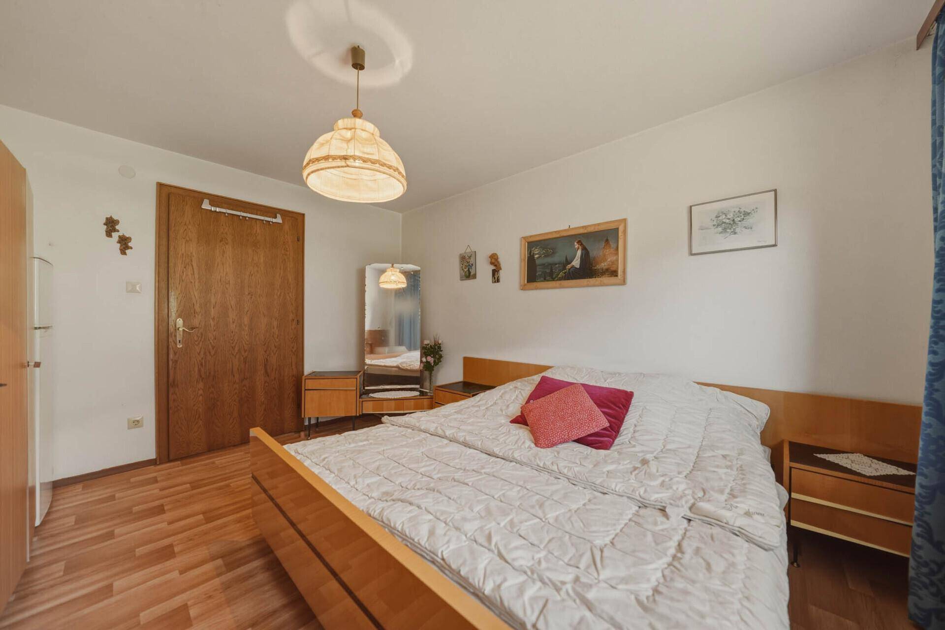 Schlafzimmer mit Doppelbett, Holzmöbeln und Laminatboden in einem hellen Raum.