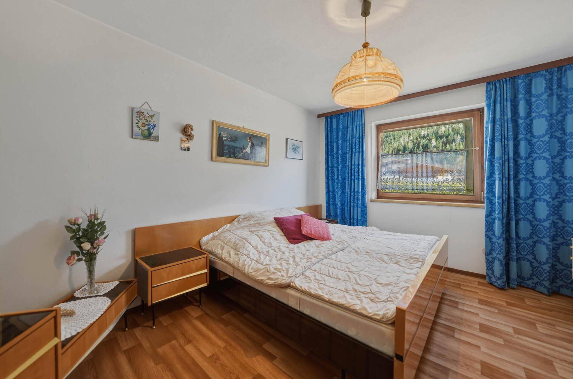 Helles Schlafzimmer mit Doppelbett, blauen Vorhängen und Blick auf die grüne Umgebung.