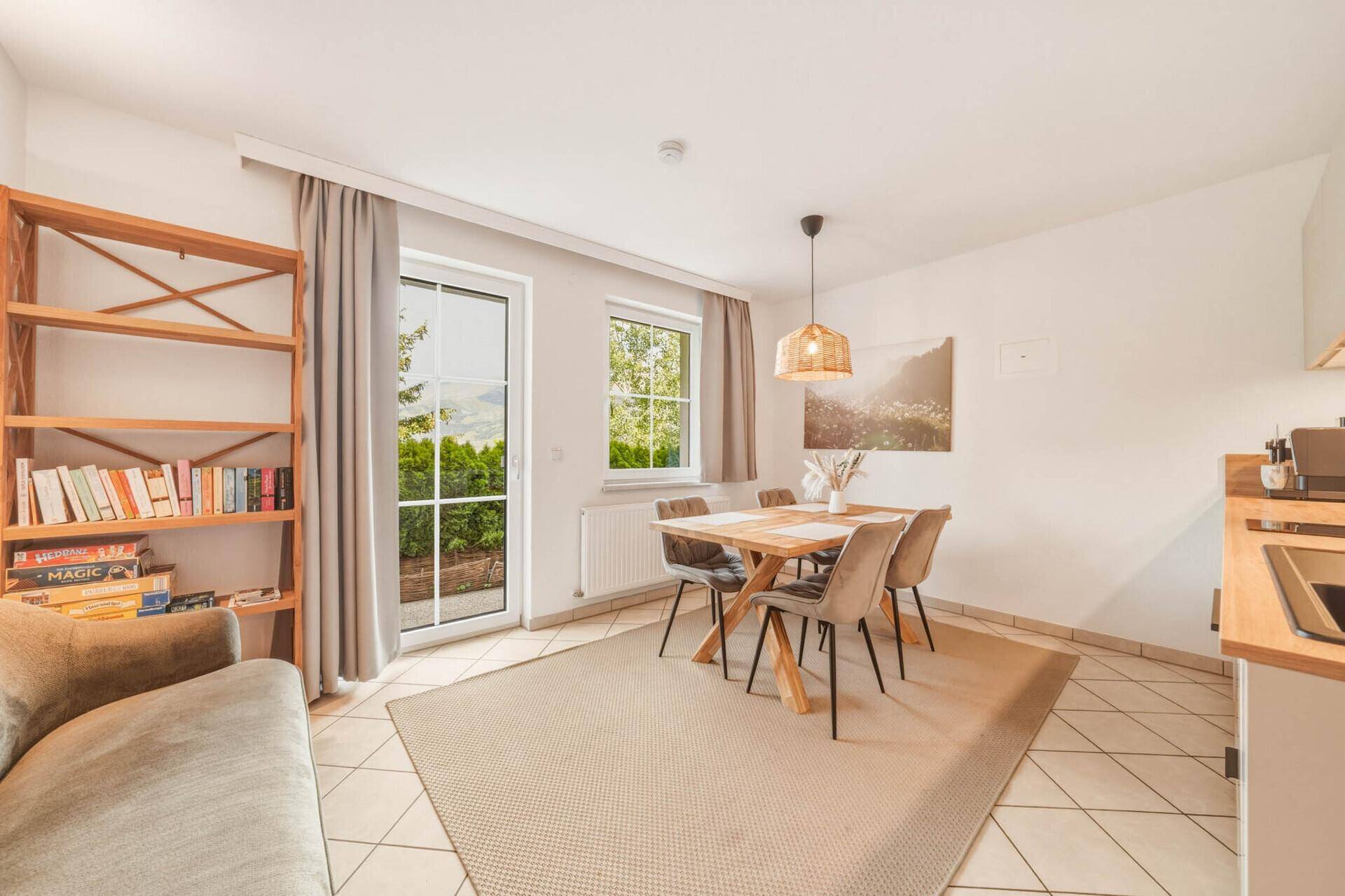 Heller Wohn-Essbereich mit Sofa, Bücherregal, Esstisch und Zugang zu einem Außenbereich.