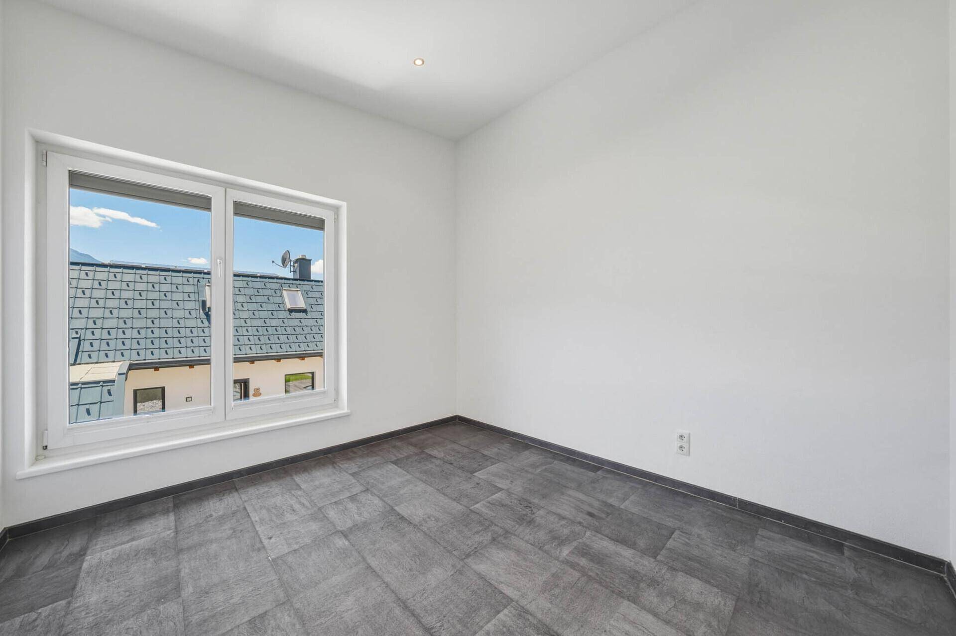 Freundliches Zimmer mit grauen Fliesen und einem großen Fenster, das viel Tageslicht hereinlässt.