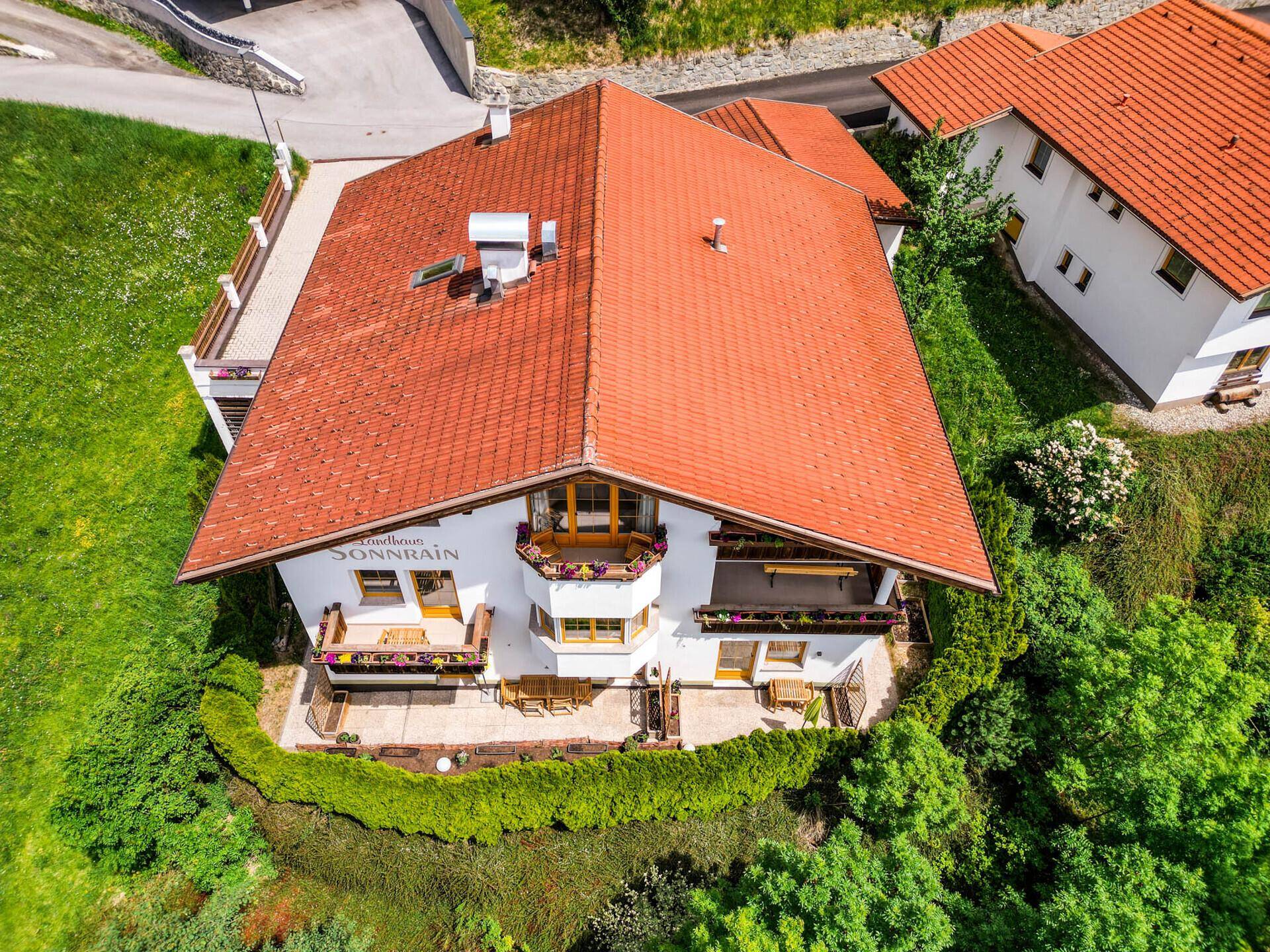 Draufsicht des Hauses mit rotem Ziegeldach, umgeben von grünen Bäumen und Wiesen.