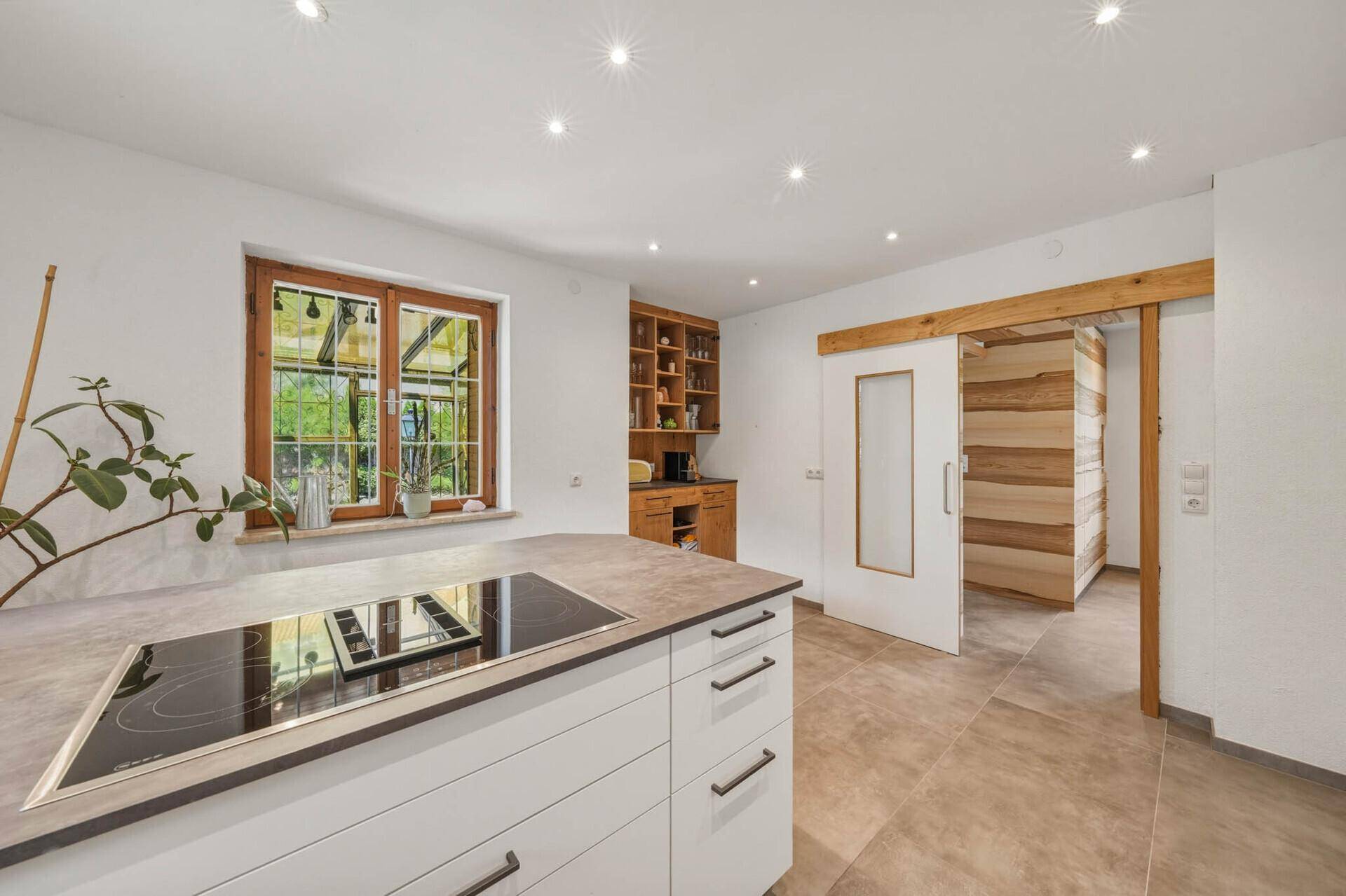 Moderne Küche mit Kochinsel, Holzelementen und Zugang zu einem weiteren Raum mit Holzverkleidung.