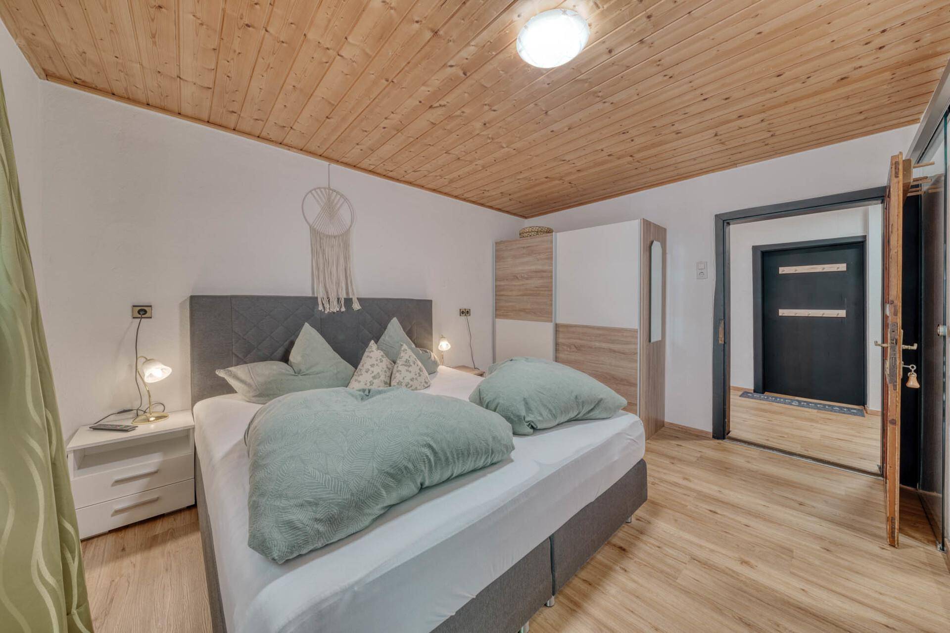 Helles Schlafzimmer mit Holzbalkendecke, Doppelbett und modernem Kleiderschrank.