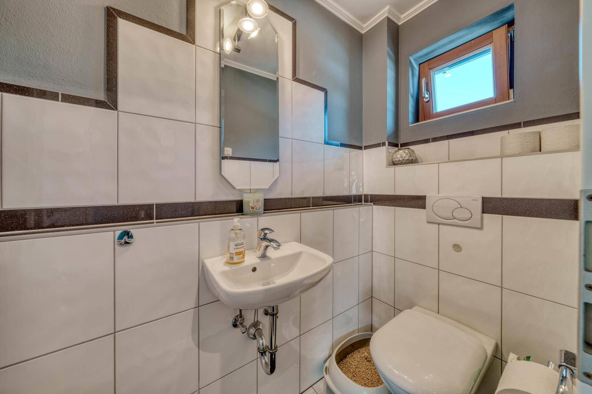 Kleines Gäste-WC mit weißen Fliesen, Fenster und modernem Waschbecken.
