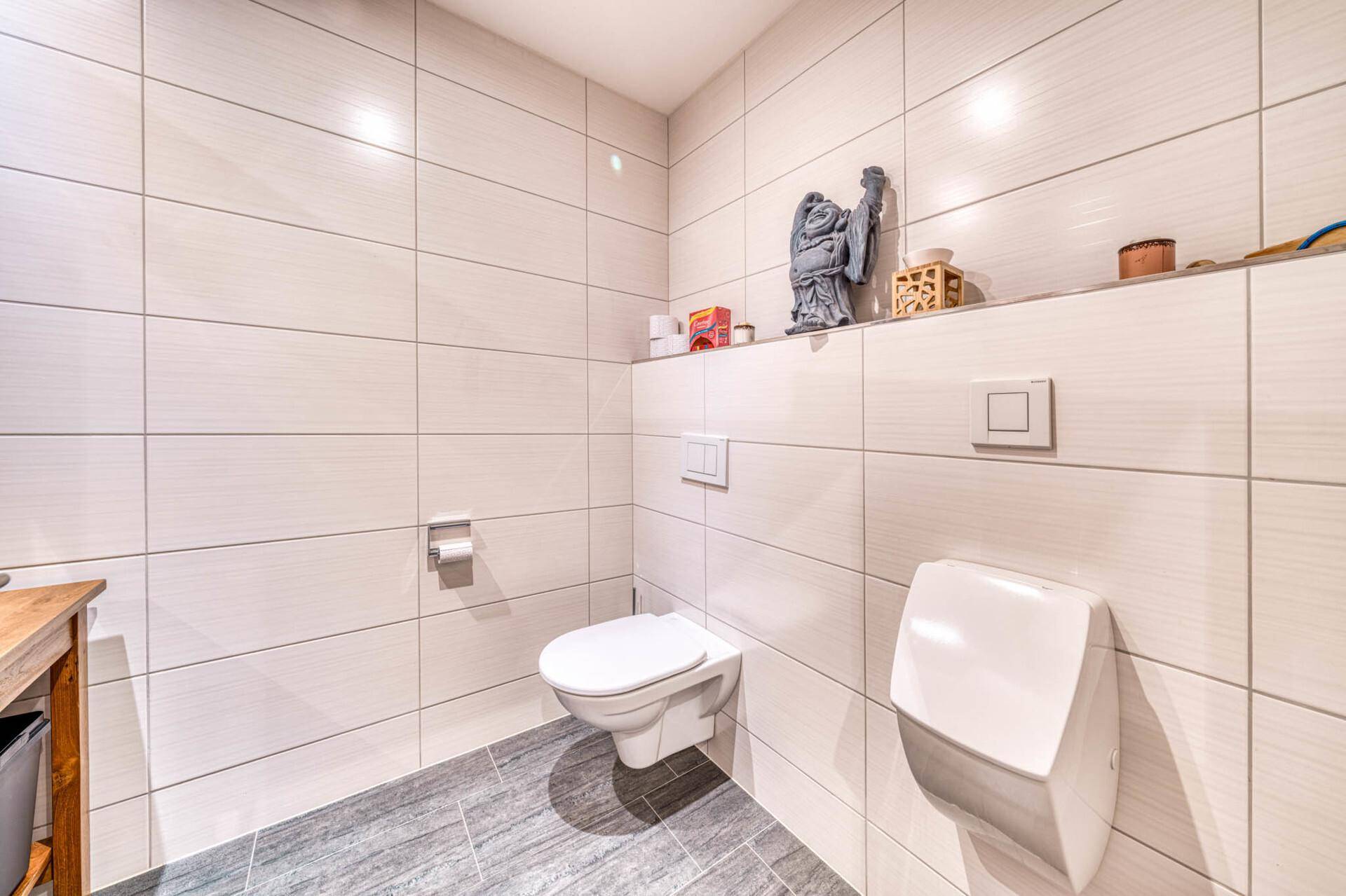 Helles Gäste-WC mit weißen Fliesen, wandhängendem WC und Urinal.