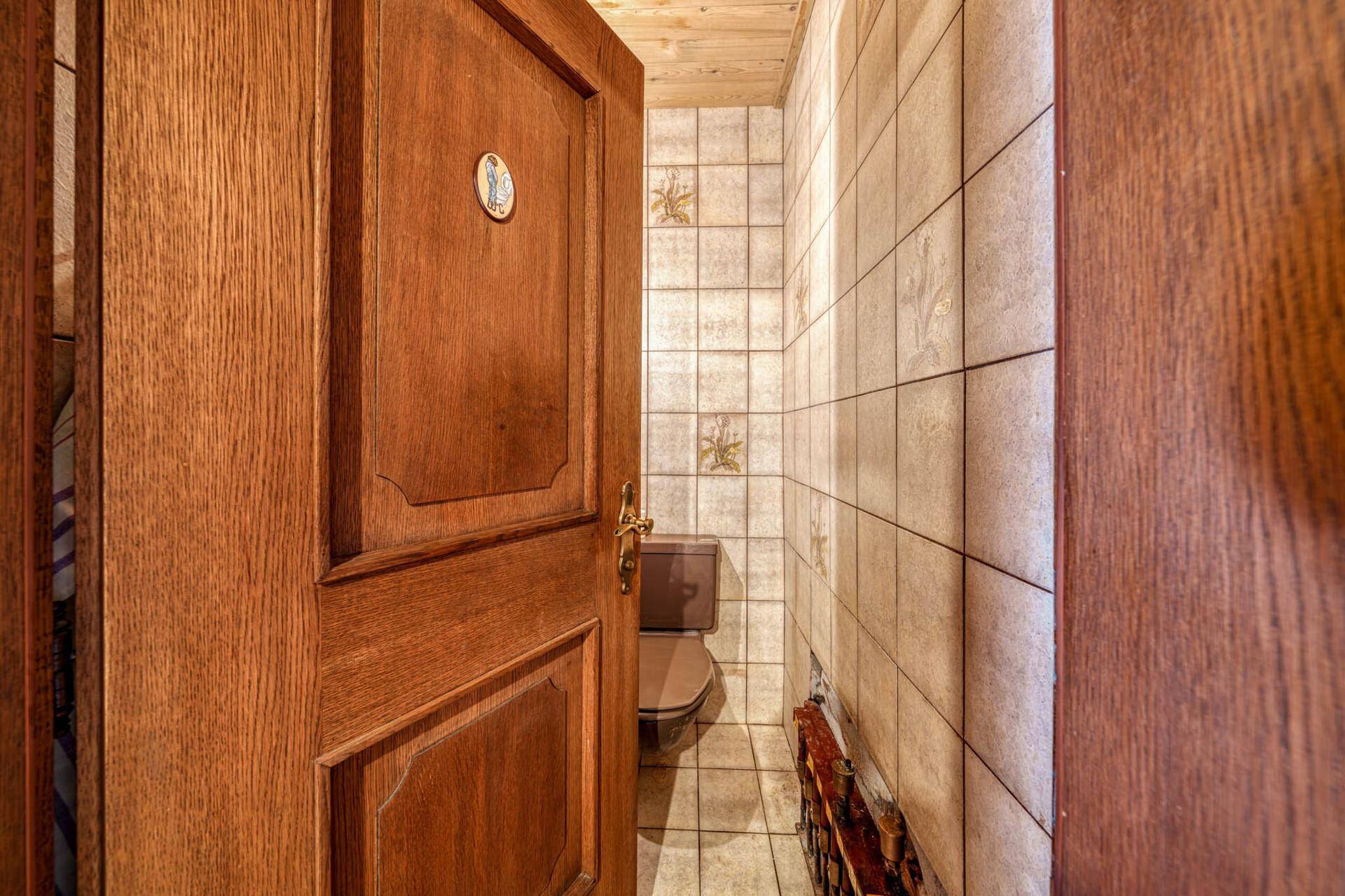 Kleines Gäste-WC mit braunen Fliesen und Holzdecke, durch eine offene Tür sichtbar.