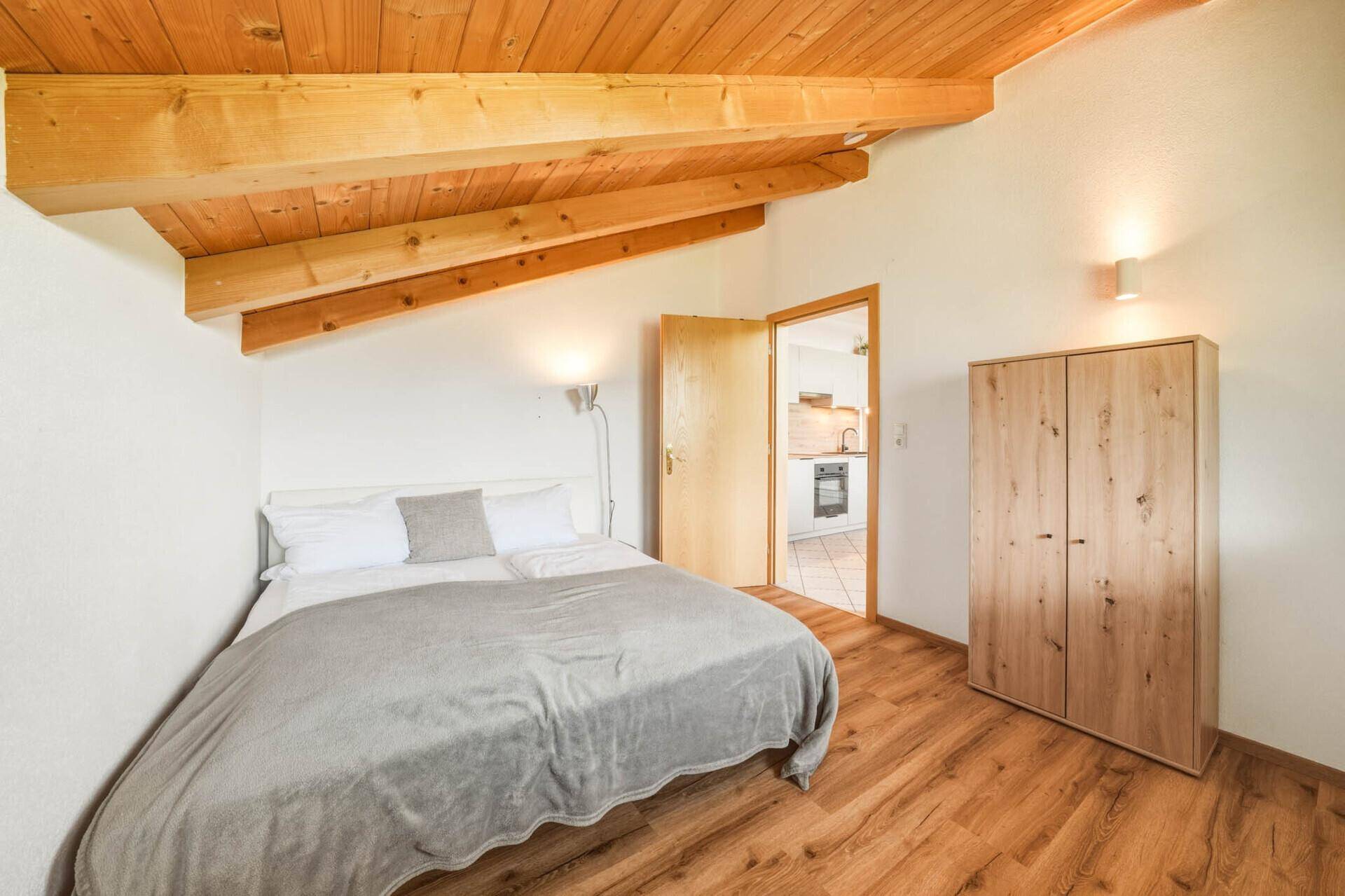 Schlafzimmer im Dachgeschoss mit Holzbalkendecke, Holzboden und Zugang zur Küche.