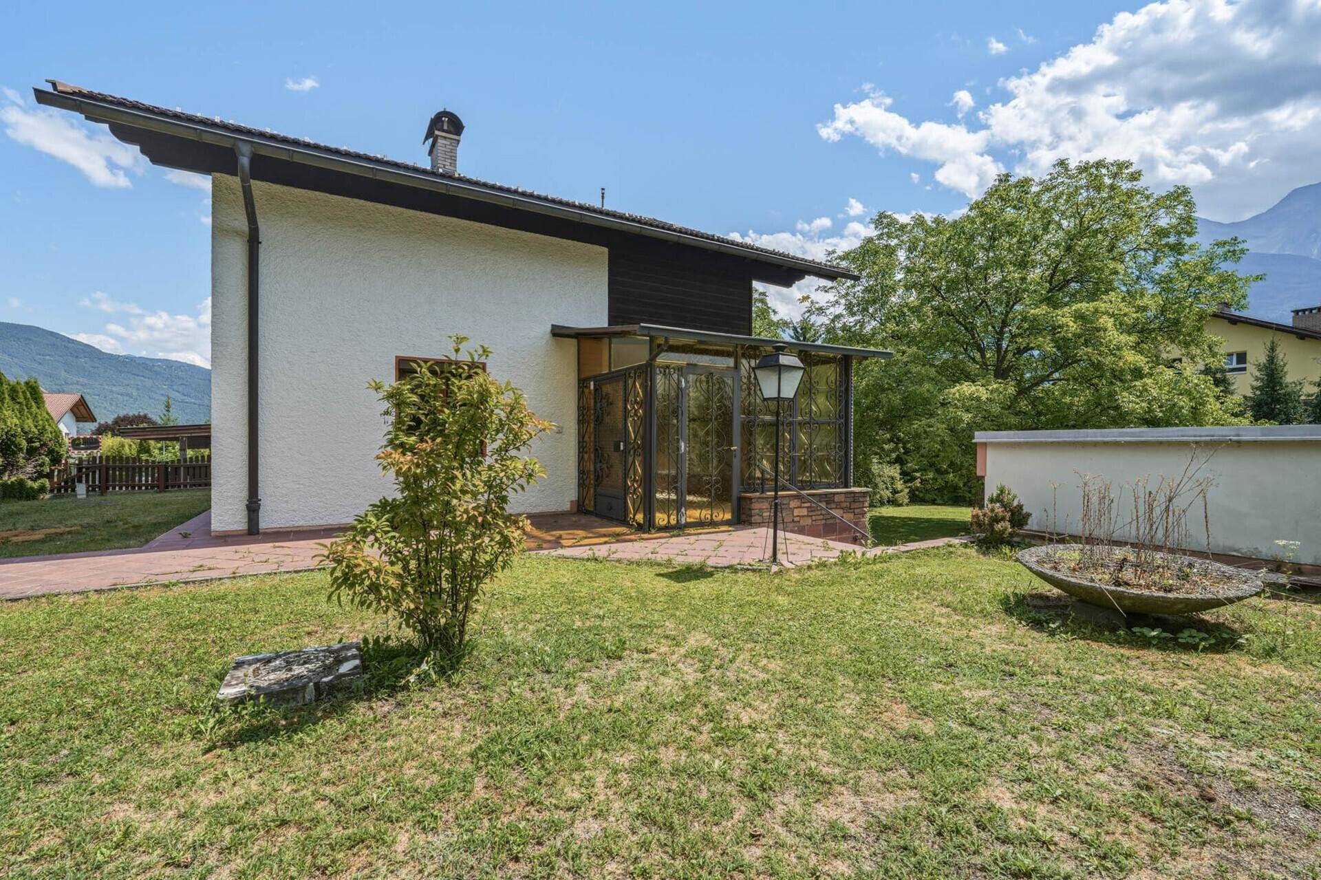 Gepflegter Garten mit Rasenfläche und dem Haus mit Wintergarten unter blauem Himmel.