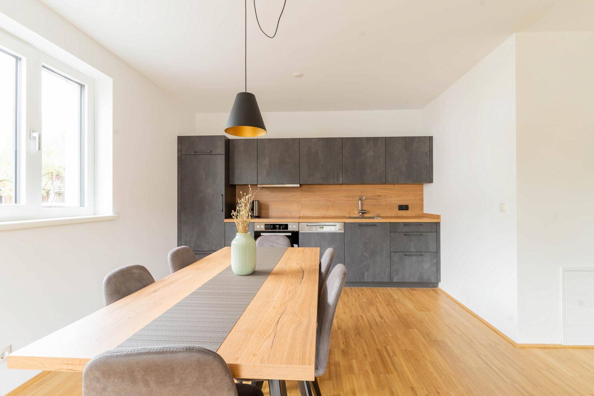 Moderne Küche mit grauen Fronten, Holzarbeitsplatte und Esstisch im offenen Bereich.