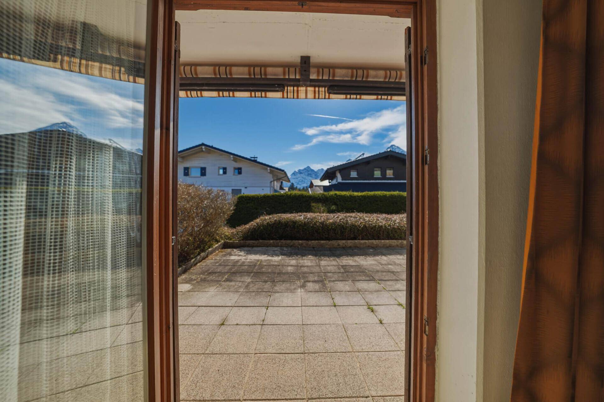 Blick von der Terrasse auf die umliegende Berglandschaft und benachbarte Häuser.