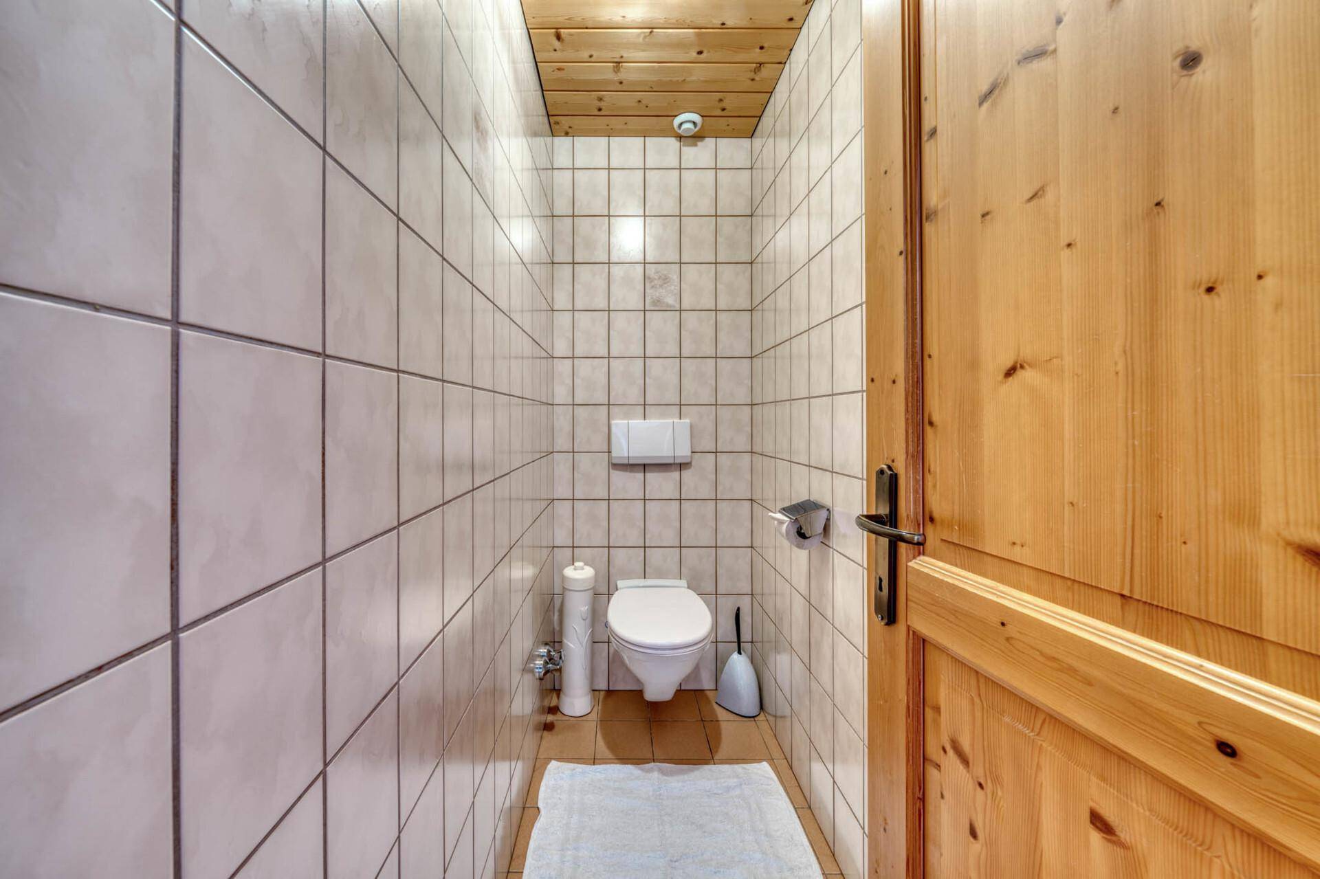 Kleines, vollständig gefliestes WC mit Toilette und Holzdecke.