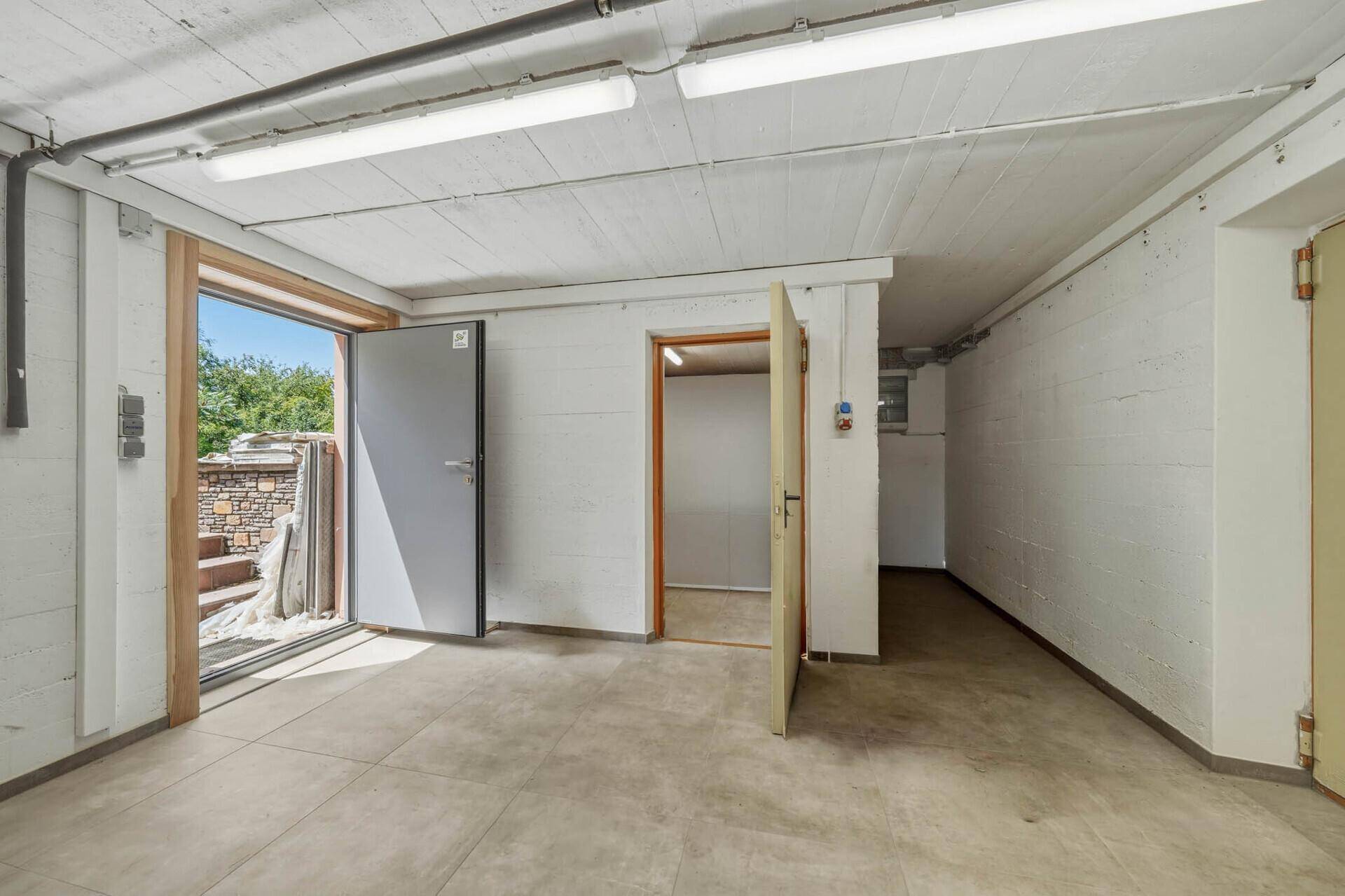 Heller Kellerraum mit Betonboden, sichtbaren Leitungen und Zugang zum Außenbereich.
