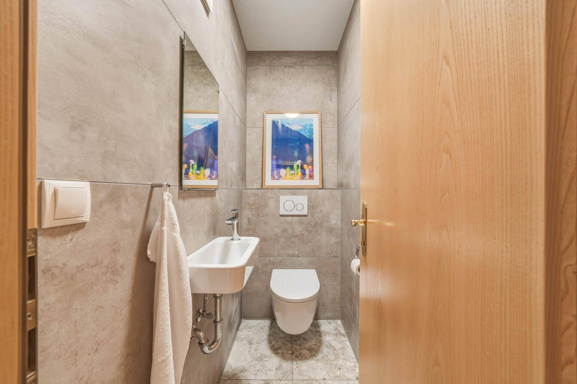 Kleines, modernes Gäste-WC mit Wand-WC, Waschbecken und grauen Fliesen.