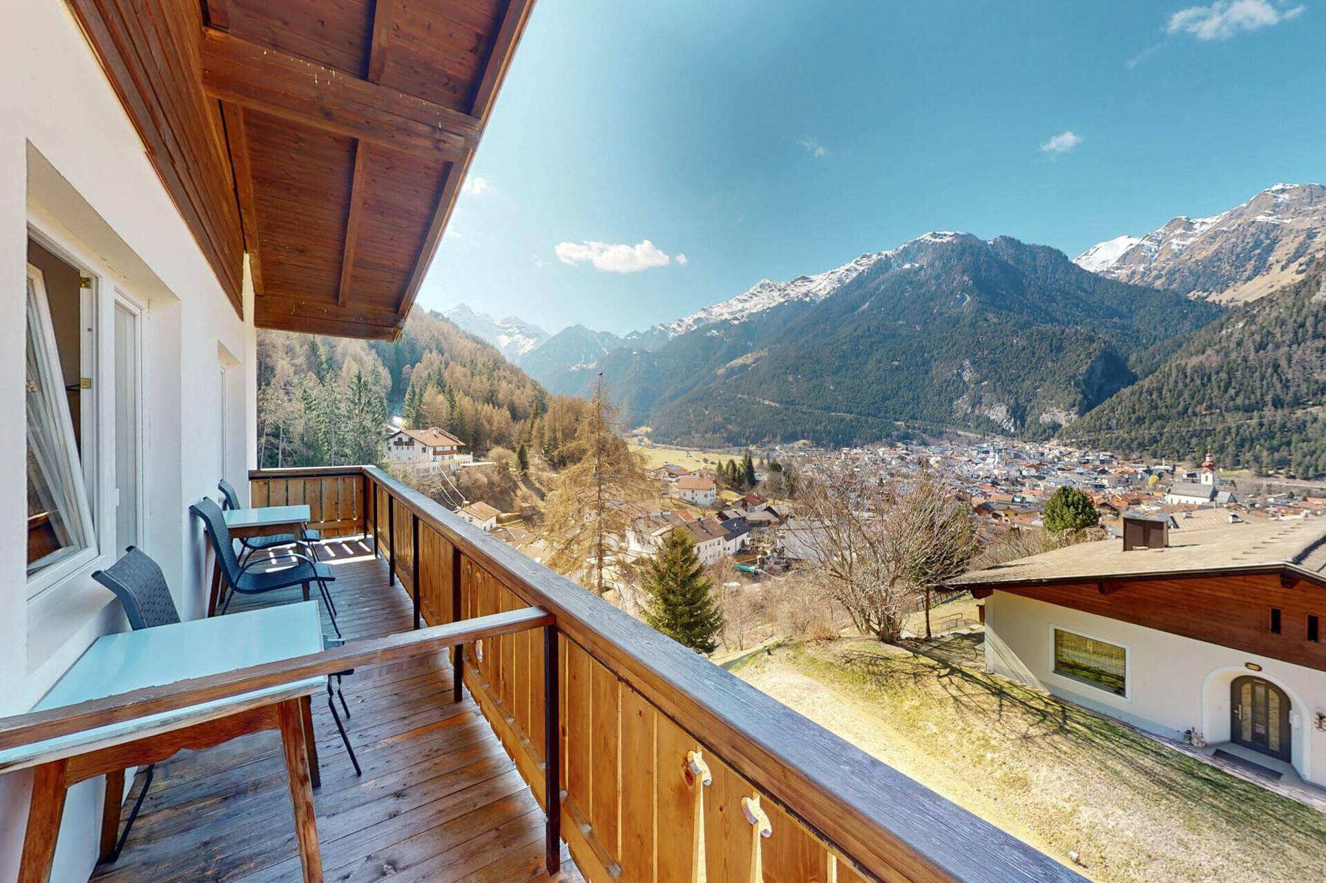 Großer Balkon mit Sitzgelegenheiten und Panoramablick auf die Berge und das Dorf.