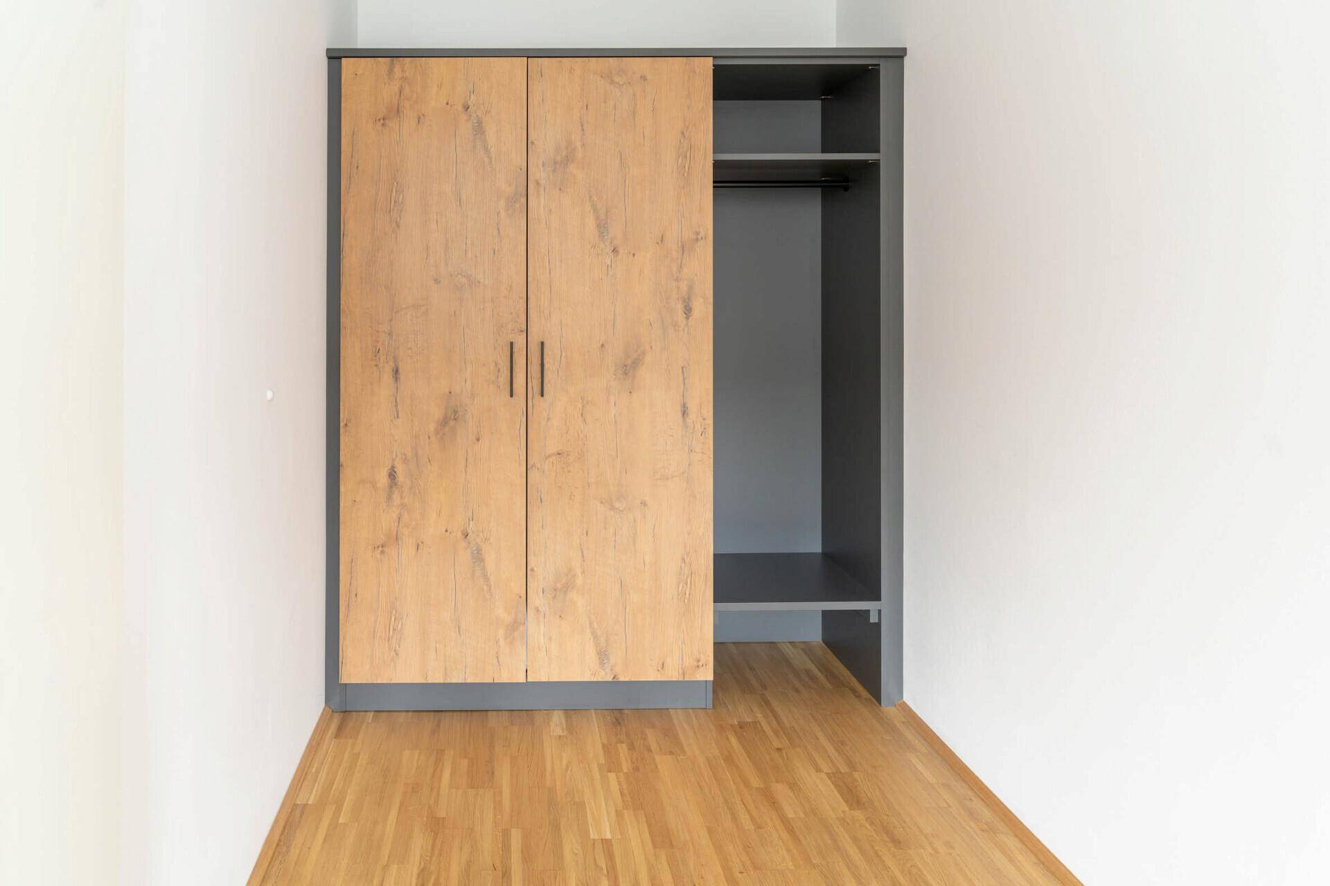 Geräumiger Kleiderschrank mit Holzfronten und offenem Regalbereich in einem Schlafzimmer.