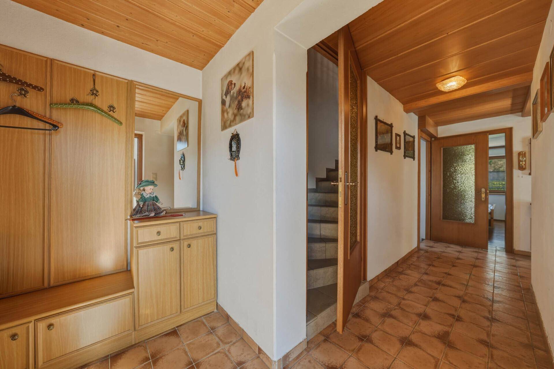 Heller Flur mit Holzdecke, Terrakottafliesen und Garderobe, führt zu weiteren Räumen.