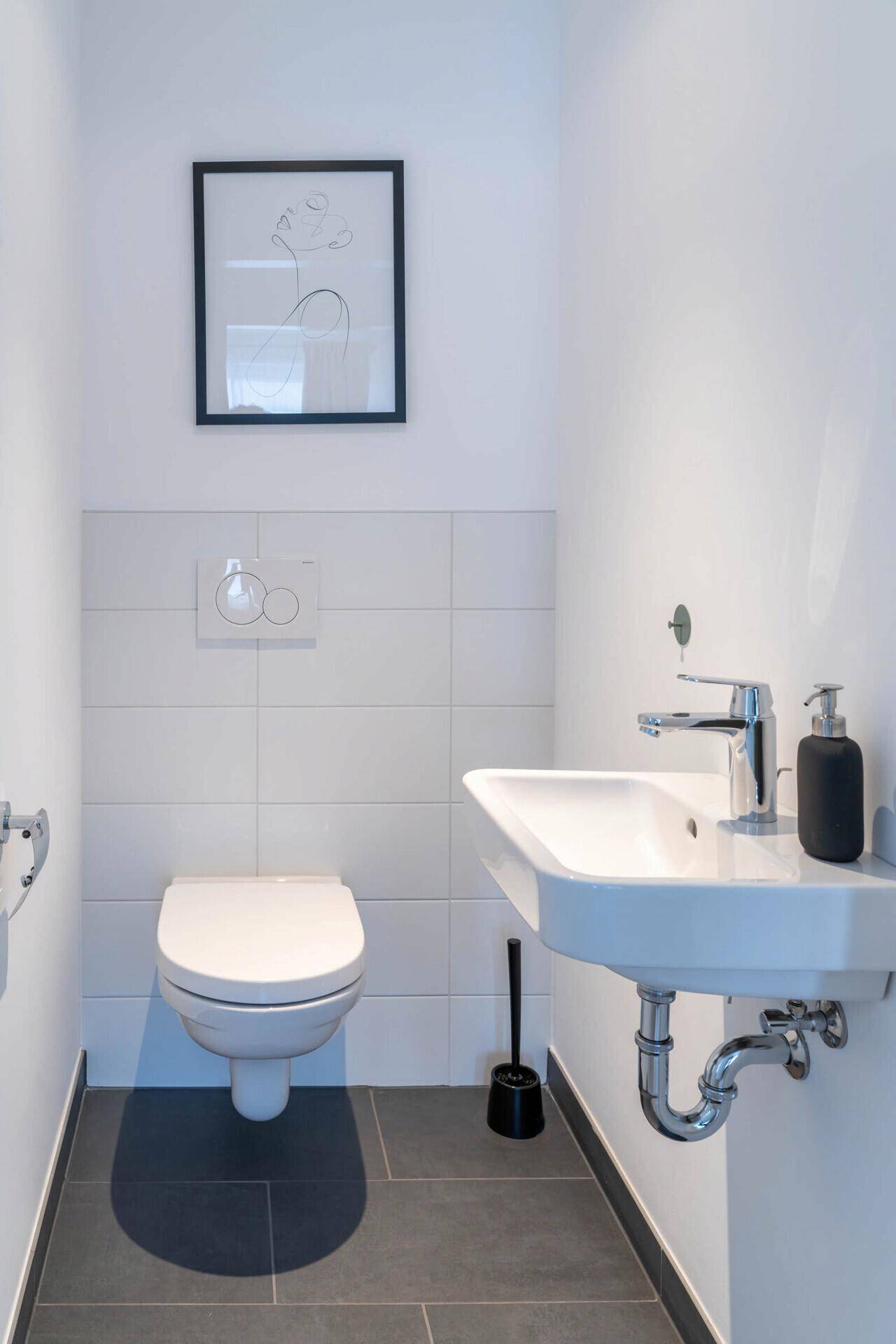 Modernes Gäste-WC mit Wand-WC, kleinem Waschbecken und dunklen Bodenfliesen.