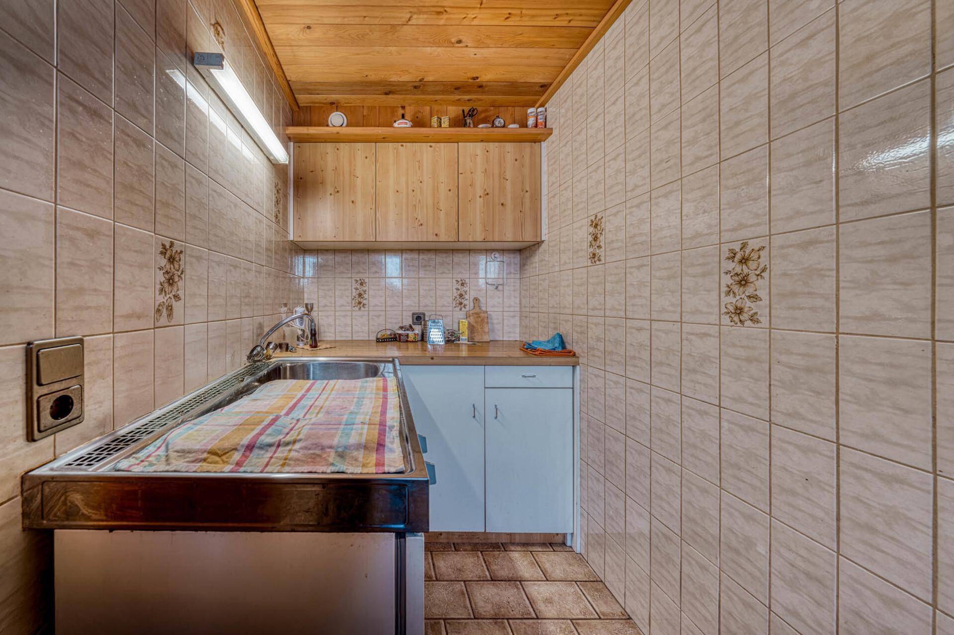 Kleine Küchenzeile mit Spüle, Kochfeld und Holzschränken in einem einfachen Stil.
