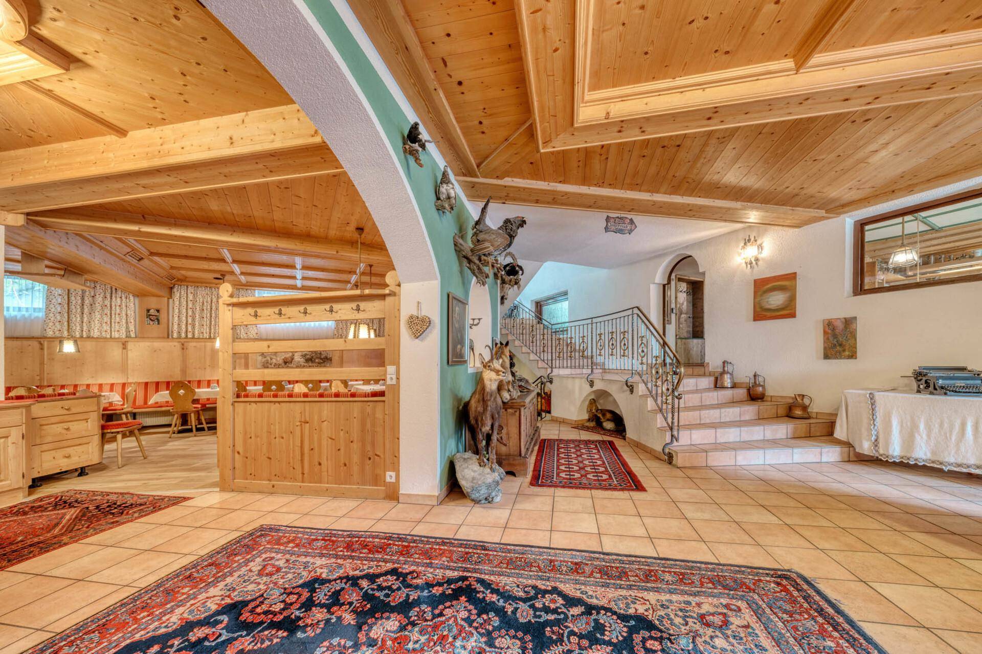 Geräumiger Flur mit Holzdecken, Fliesenboden und einer Treppe mit schmiedeeisernem Geländer.