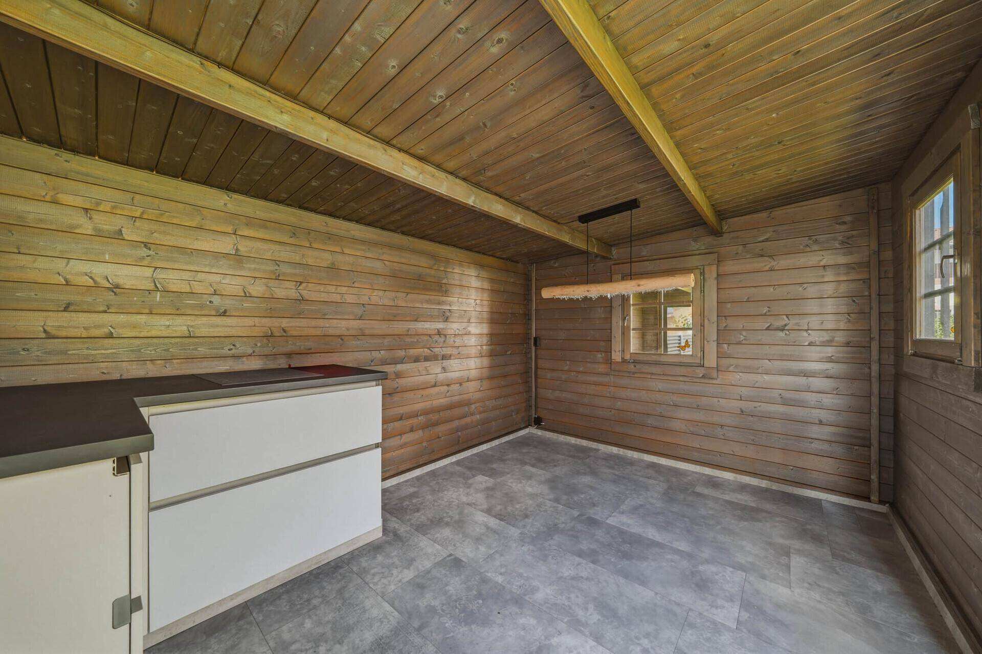 Innenansicht des Holzschuppens mit Holzvertäfelung, Fenster und einfacher Einrichtung.