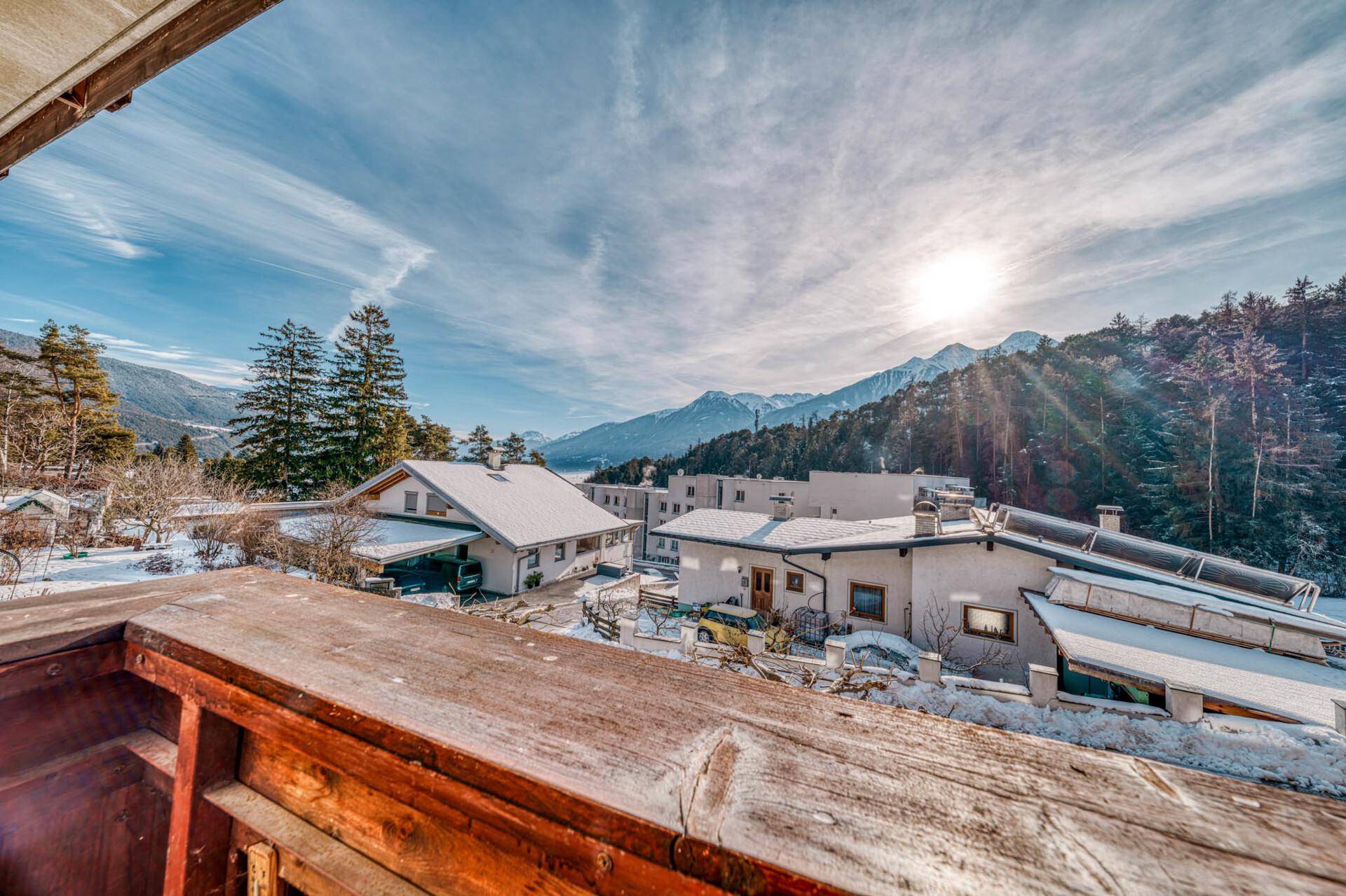 Sonniger Balkon mit Holzbalkonbrüstung und weitem Blick auf die verschneite Berglandschaft.