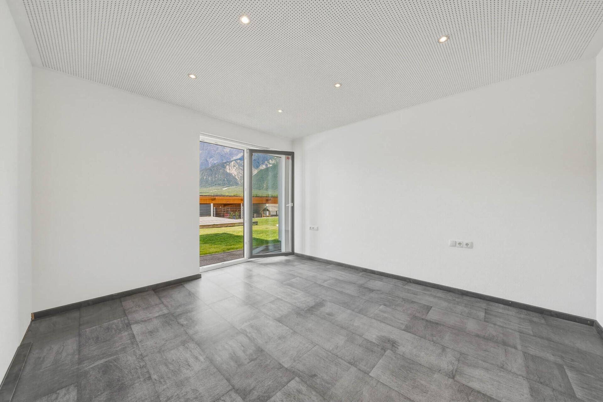 Helles Zimmer mit grauen Fliesen und einer Tür, die direkten Zugang zum Garten bietet.